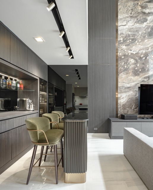 Home bar with backlit bottle display, fluted counter and olive velvet bar stools in a luxury Bangkok residence