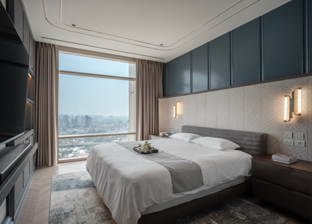 Master bedroom with deep blue overhead cabinets, textured stone headboard wall and Bangkok city view