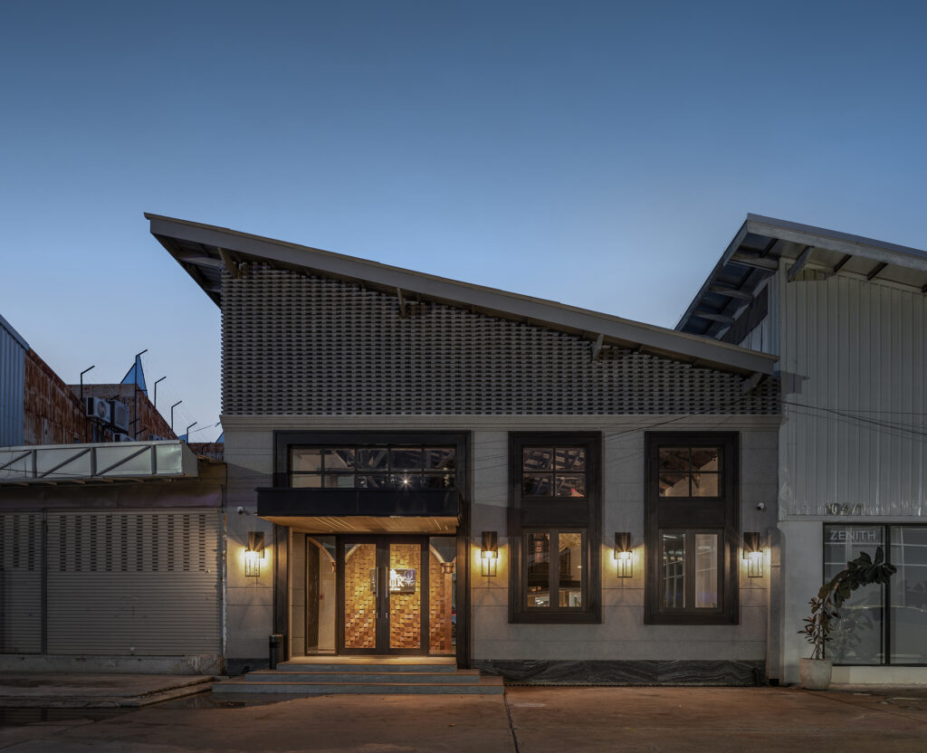 Converted warehouse facade of Kilik Social Club Bangkok with brick lattice gable and arched timber entrance at dusk