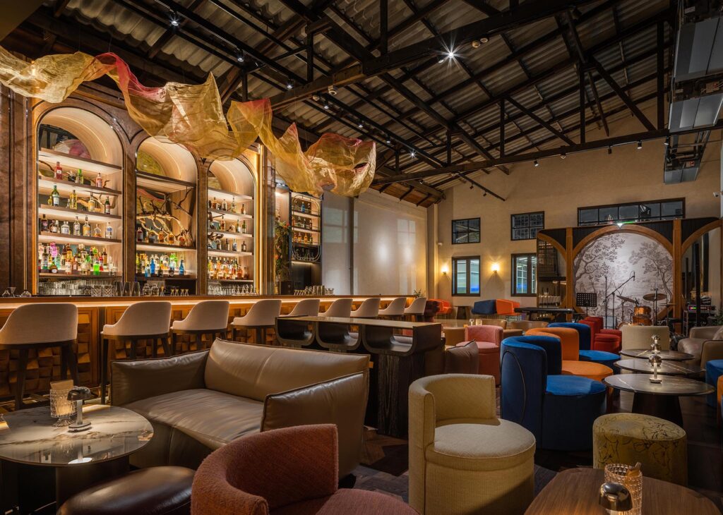 Main hall of Kilik Social Club with bar counter, stage and mixed lounge seating under an exposed steel roof