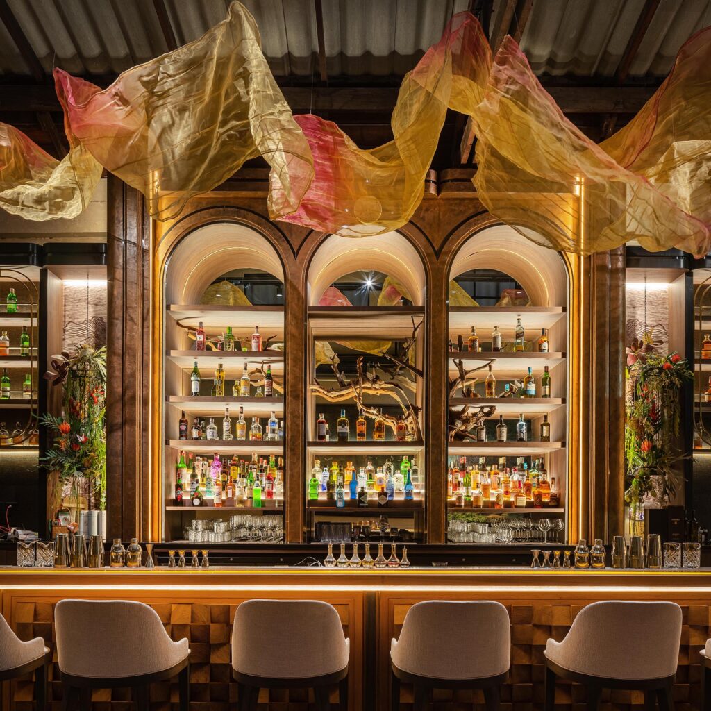 Arched back bar of Kilik Social Club with backlit bottle shelves and hand-dyed organza fabric installation