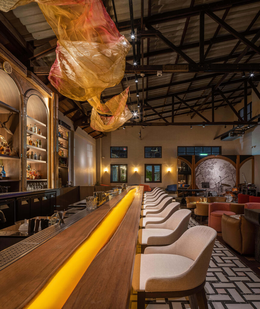 Live-edge timber bar counter with recessed amber lighting at Kilik Social Club Bangkok