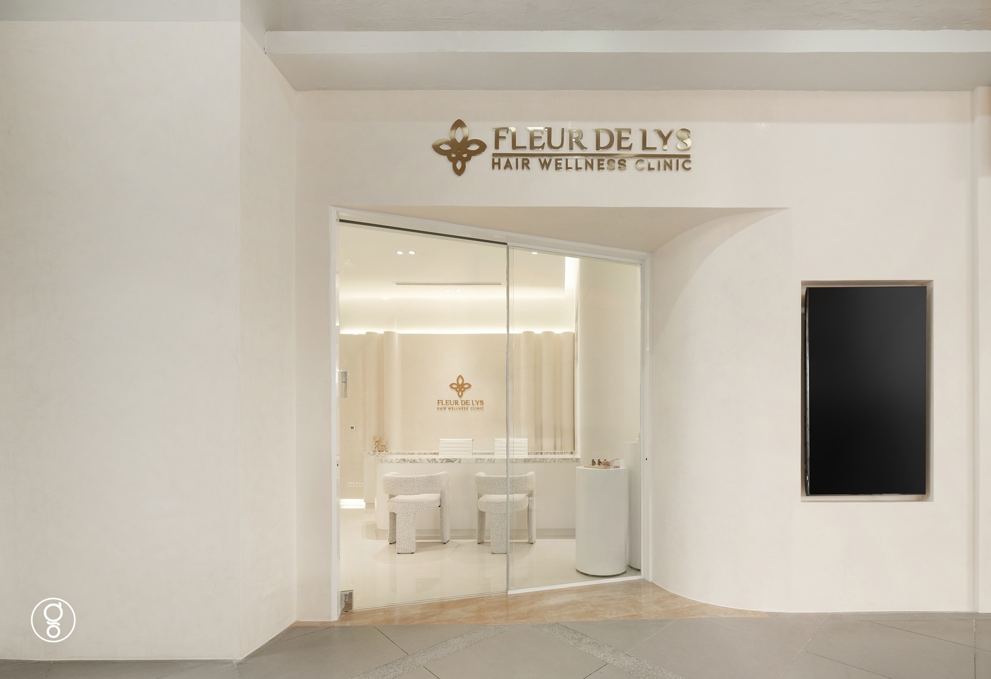 Fleur De Lys hair clinic shopfront at K Village, a cream plaster wall with a brass sign and a full-height glass entrance opening onto the reception