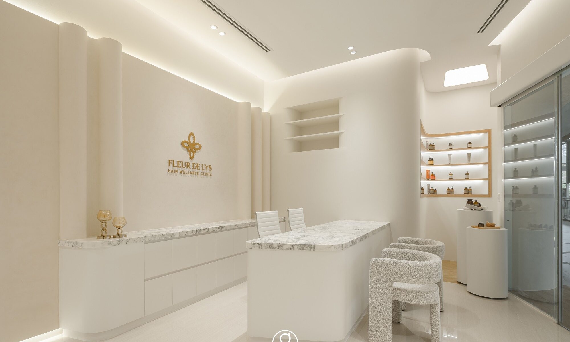 Fleur De Lys Hair Wellness Clinic, K Village — white reception with marble consultation counter, sculpted plaster walls and backlit product niches, by Gratitude Design
