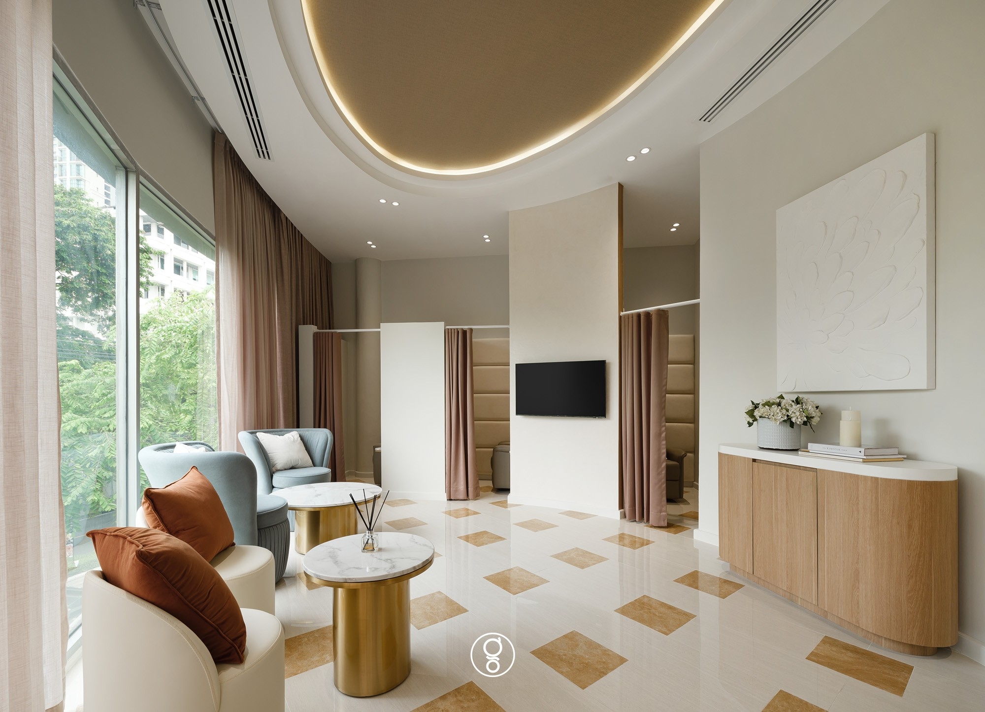 Clinic waiting lounge with a gold illuminated ceiling disc, blue and cream tub chairs, brass and marble side tables and a travertine chequer floor