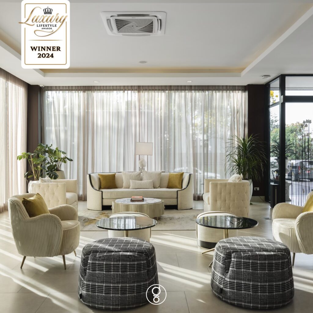 Daylit lobby lounge at La Miniera Pool Villas with fluted armchairs, checked ottomans and sheer drapery