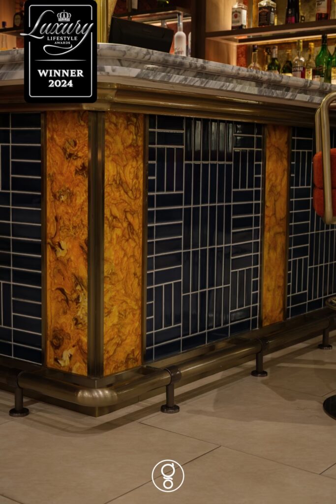 Detail of navy stack-bond glazed tile bar front with brass banding and burl wood panels