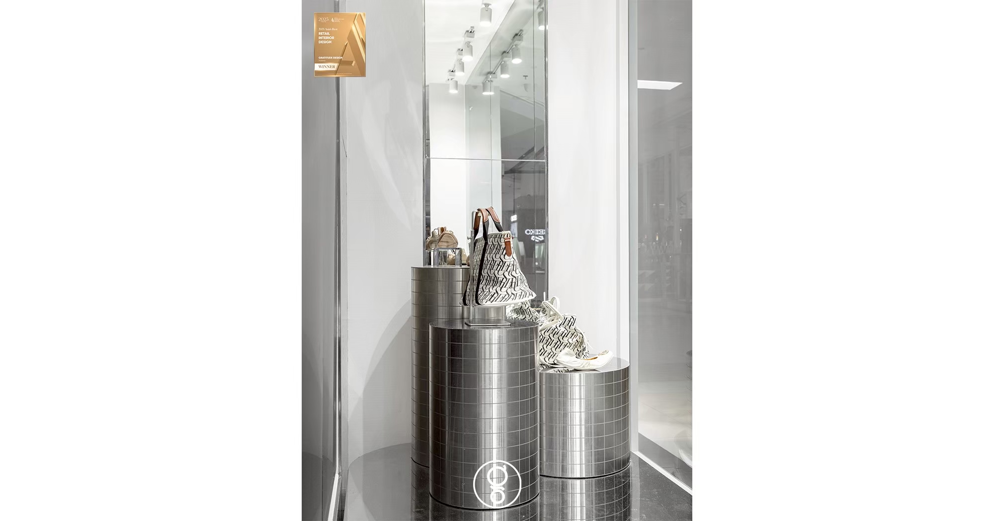 Window display at SHU Fashion Island with brushed stainless cylinders of three heights set against a full-height mirror
