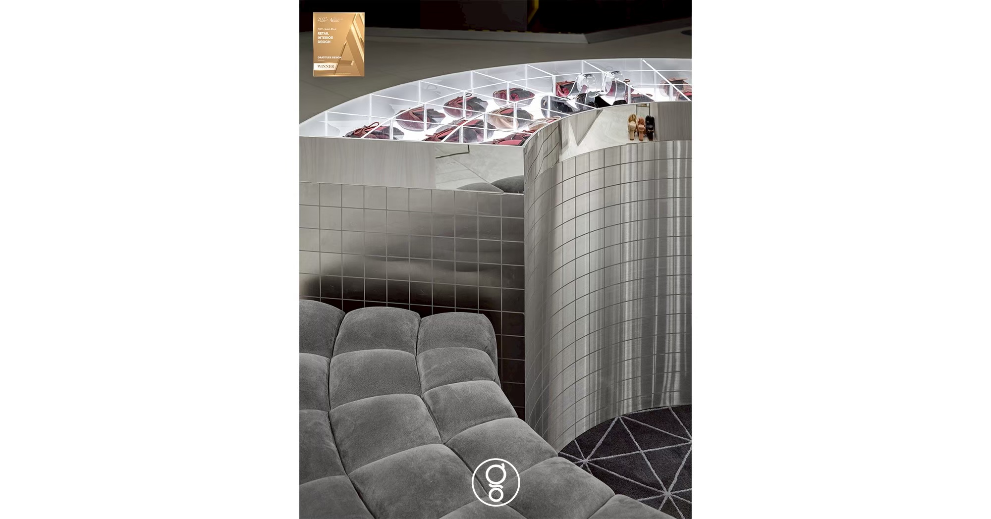 Channel-tufted grey velvet seating curved around a metallic mosaic display island with a lit acrylic vitrine top