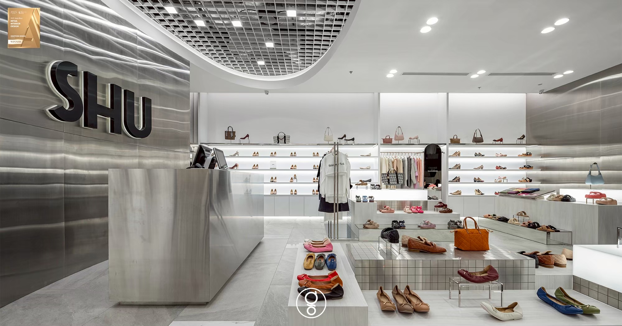 Brushed stainless steel feature wall at SHU Fashion Island worked into a shallow horizontal ripple, with a halo-lit logo above the cash desk