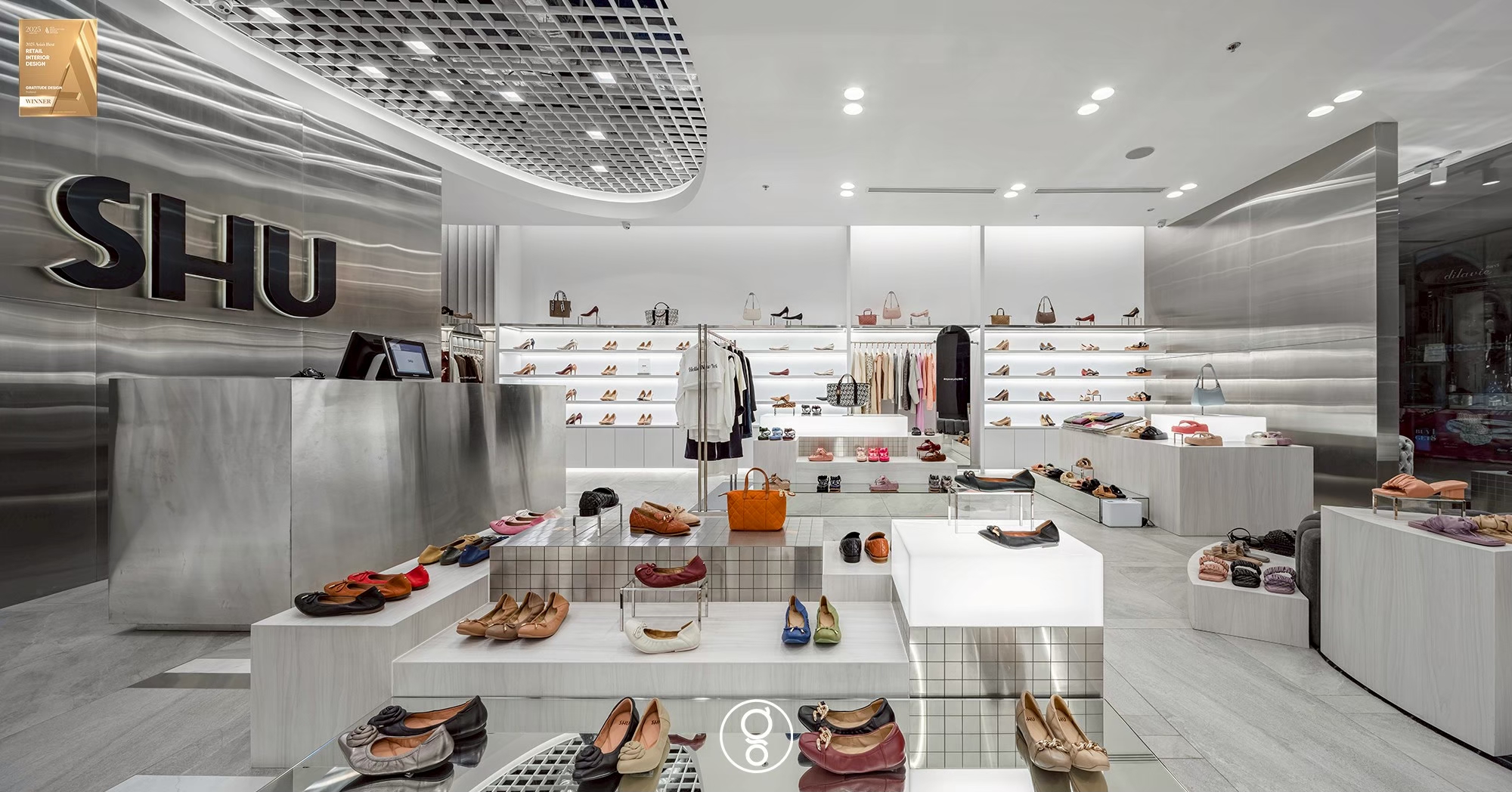 Shoe store interior design at SHU Fashion Island in Bangkok, a rippled stainless steel wall carrying a halo-lit logo above a stainless cash desk