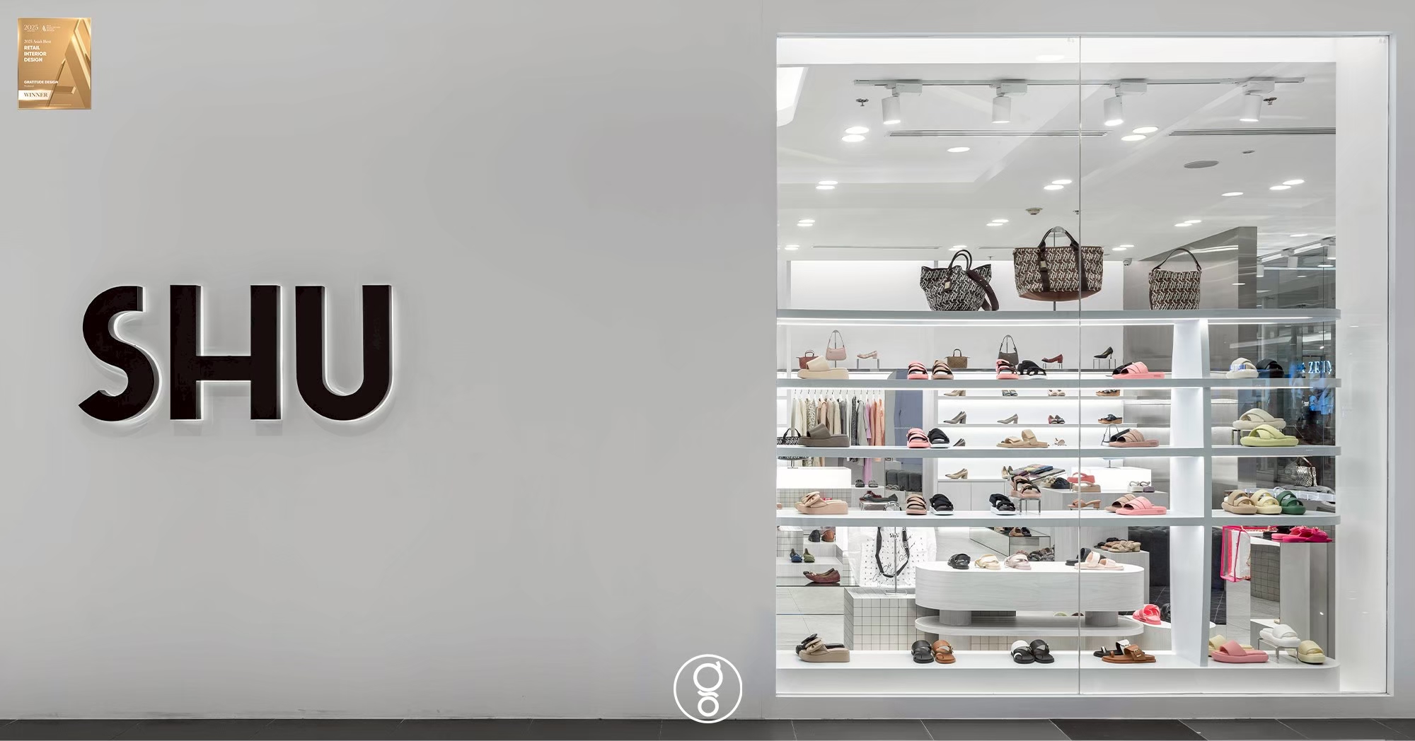 Black SHU lettering on a white pier beside a glazed window display of shoes and bags at Fashion Island