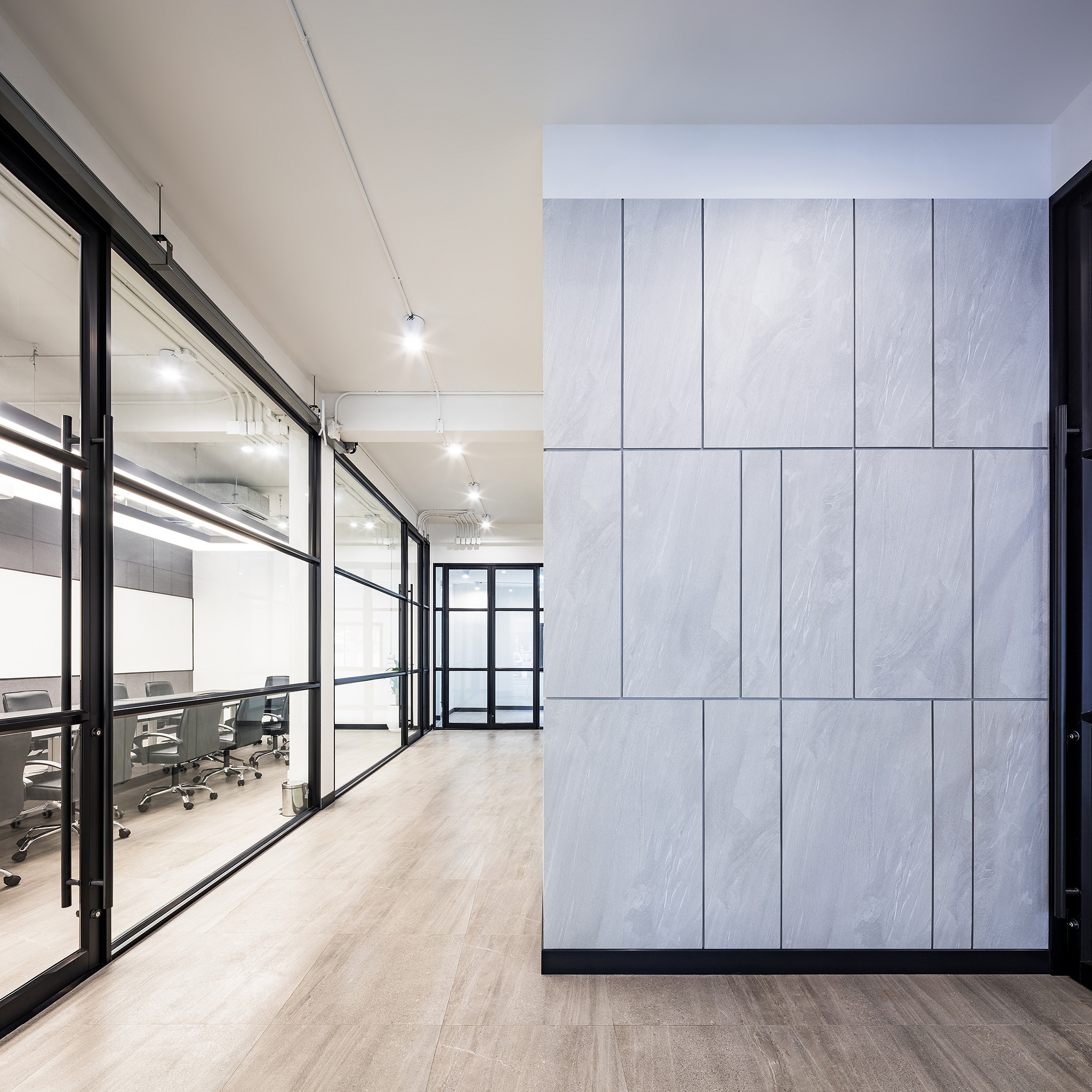 Head office interior design in Bangkok — stone-panelled core wall facing glazed meeting rooms