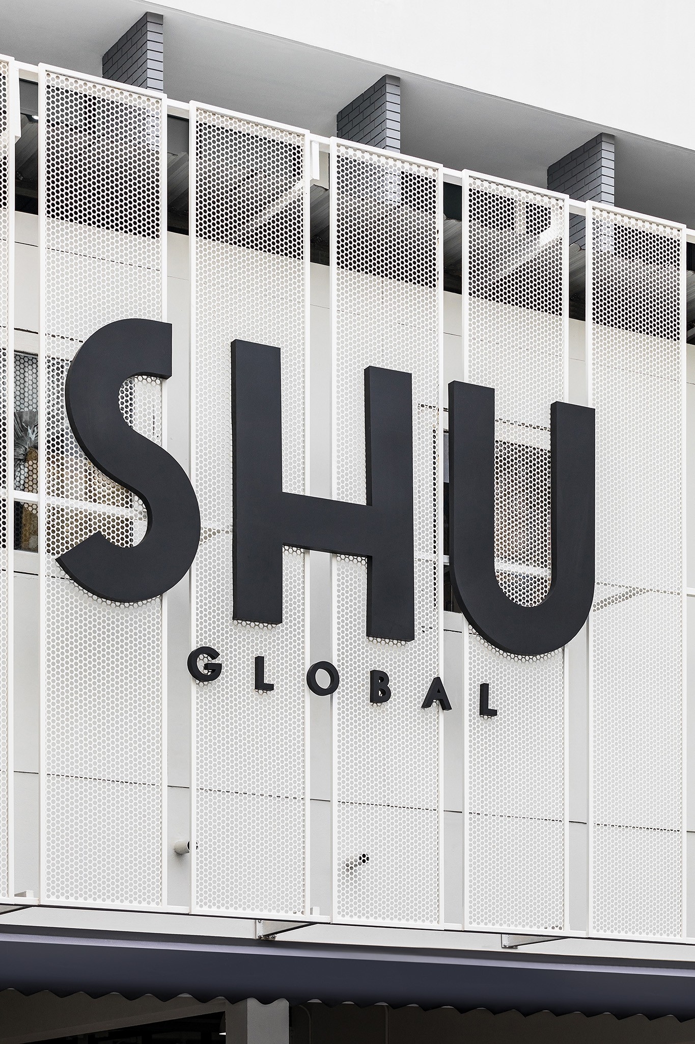 Flagship store facade in Bangkok — black brand lettering standing proud of a perforated white metal screen
