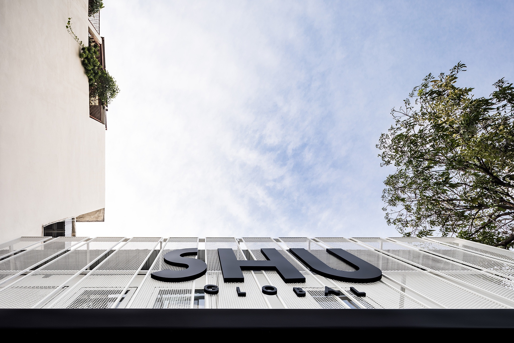 Flagship store facade in Bangkok — perforated screen seen from below against the sky