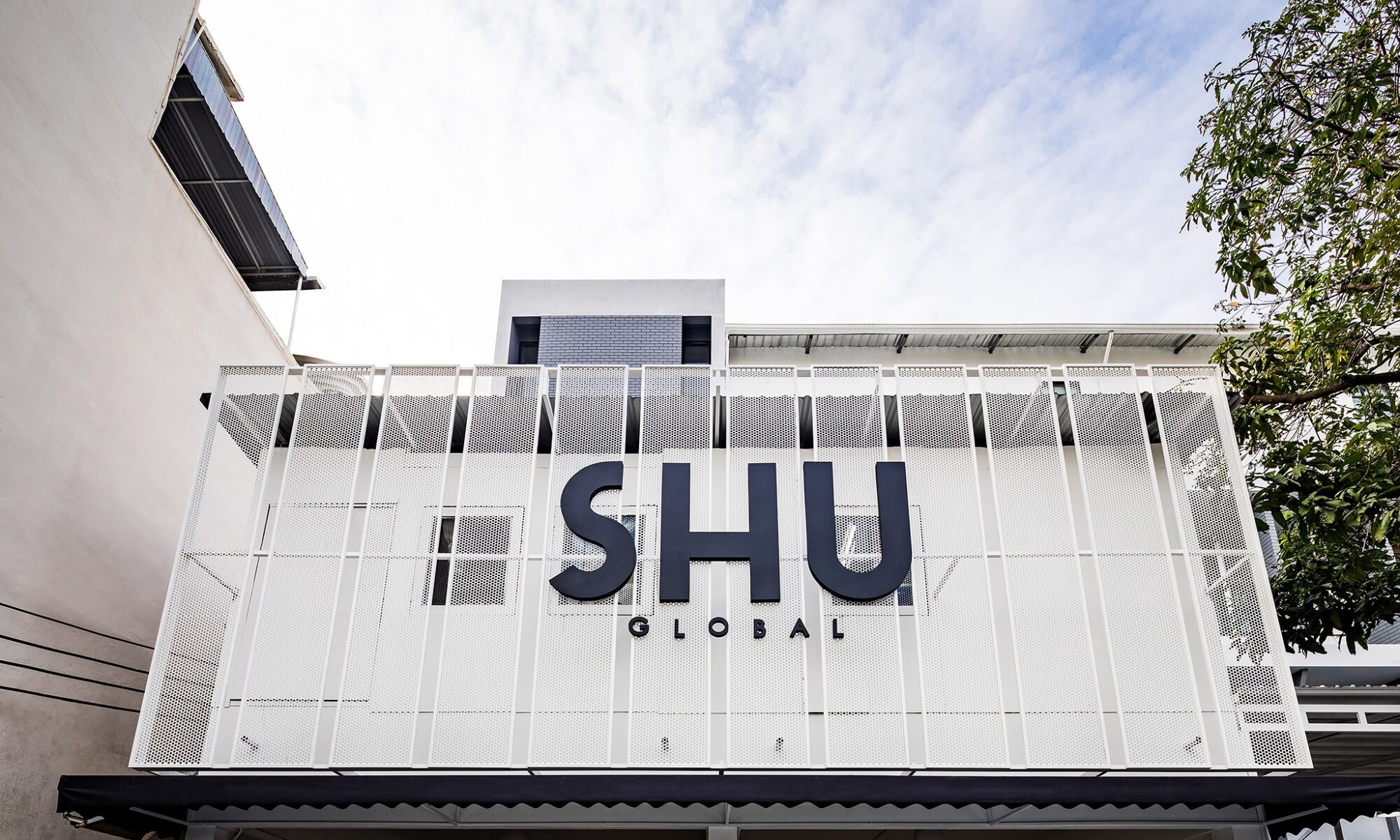 Flagship store and head office interior design for SHU in Bangkok — perforated white metal screen facade carrying the SHU Global mark
