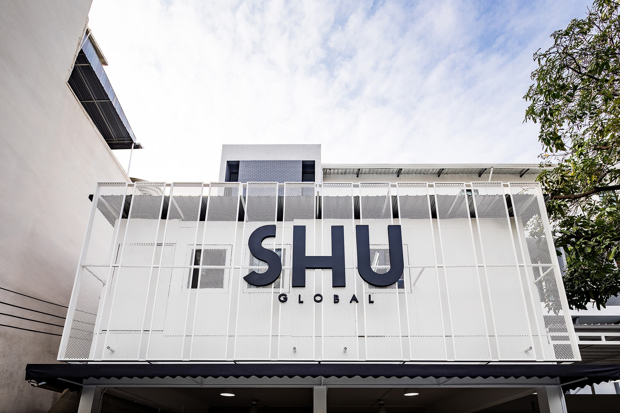 Flagship store and head office interior design for SHU in Bangkok — perforated white metal screen facade carrying the SHU Global mark