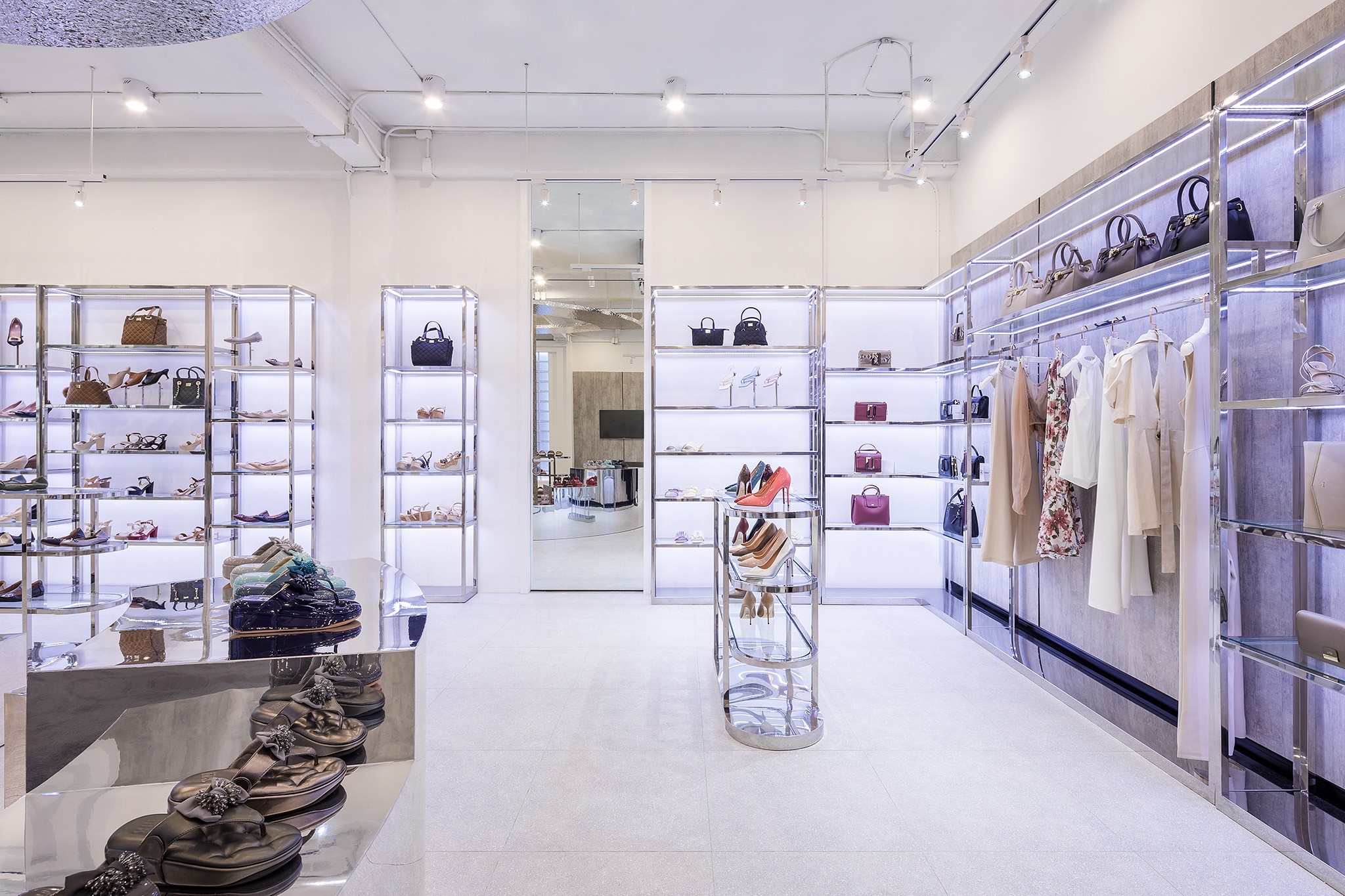Shoe store interior design in Bangkok — chrome and glass perimeter shelving with backlit panels