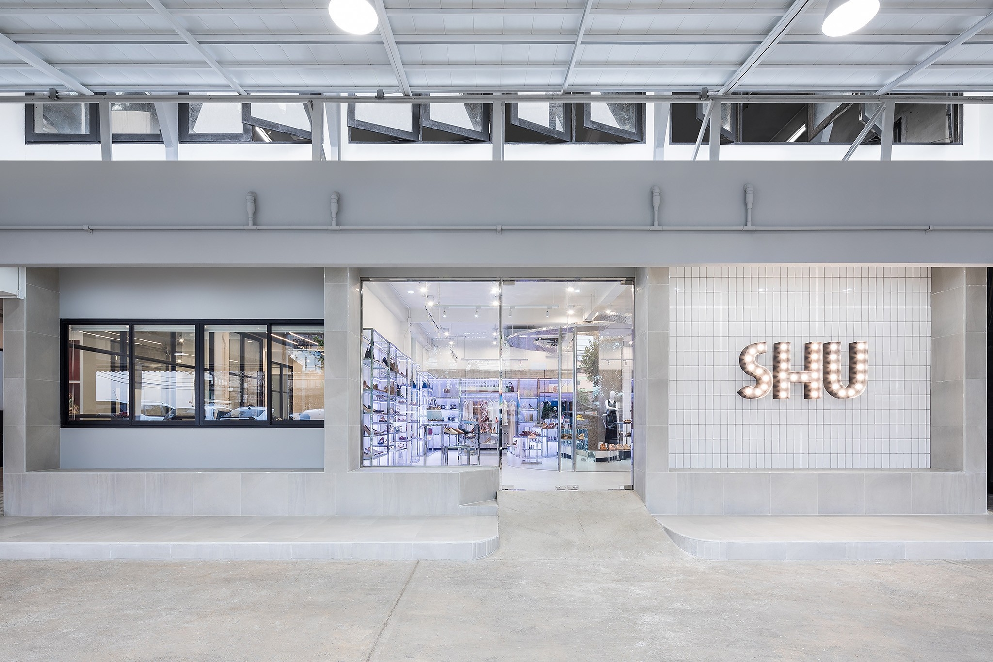 Flagship store interior design in Bangkok — concrete shopfront with marquee bulb lettering under a steel canopy