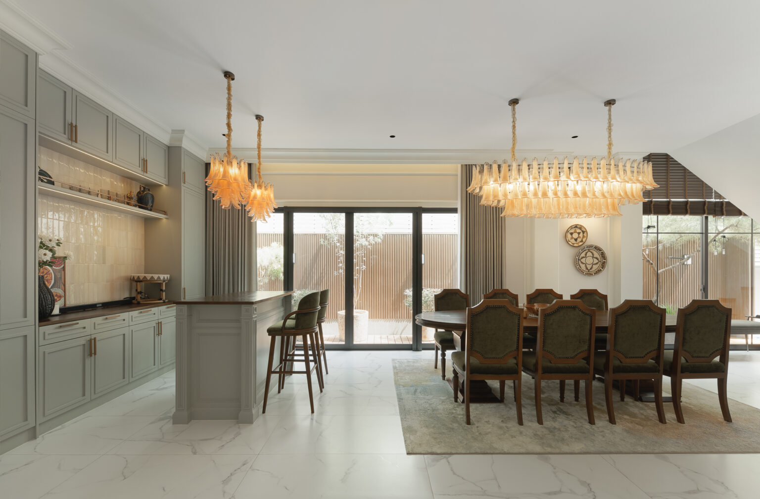 Grand Bangkok Boulevard open kitchen and dining — sage-green panelled cabinetry, zellige tile splashback, amber glass pendants and a ten-seat dining table opening to the garden