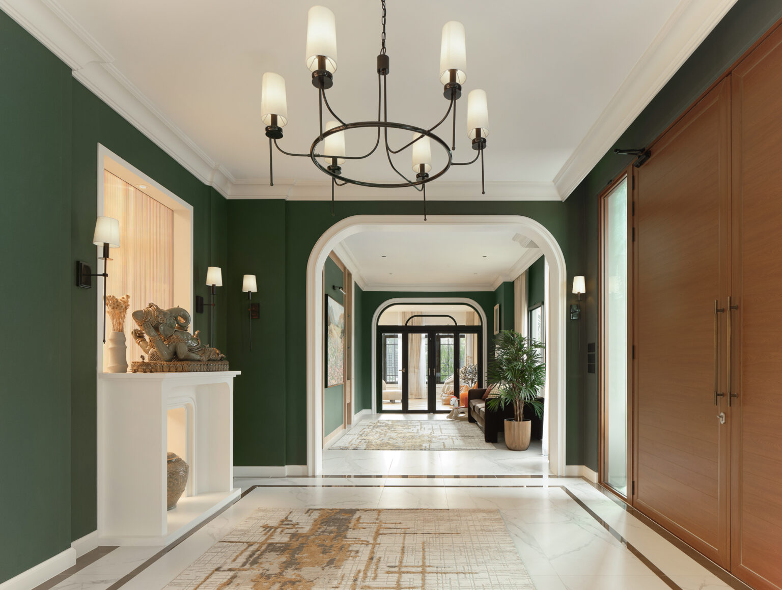 Grand Bangkok Boulevard entrance foyer — deep green walls, white cornice and arched openings, black iron chandelier, backlit niche with a Ganesha sculpture on a white console