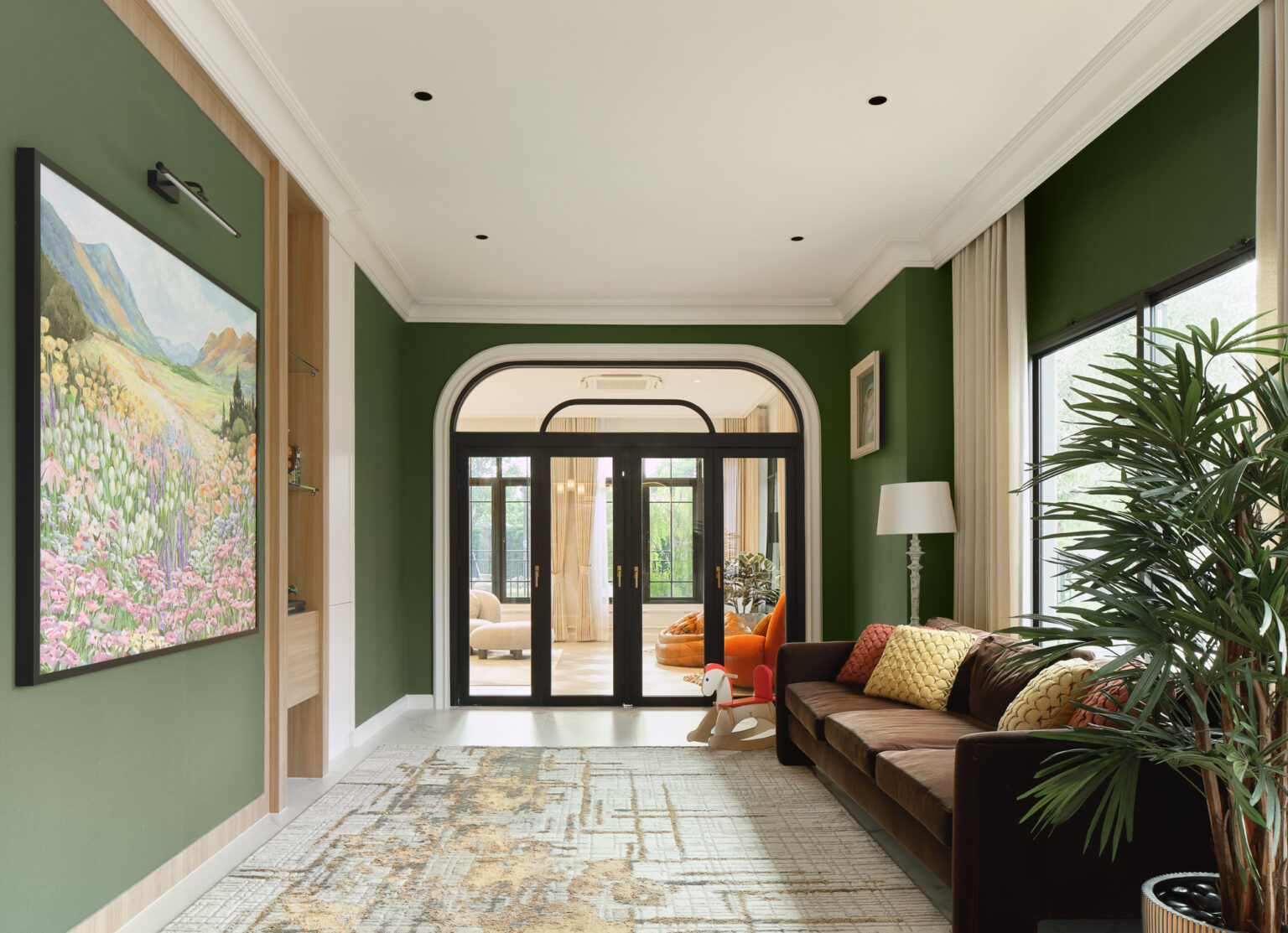 Grand Bangkok Boulevard family lounge — green walls with a landscape painting, brown velvet sofa, arched steel-framed glass doors opening to the living room
