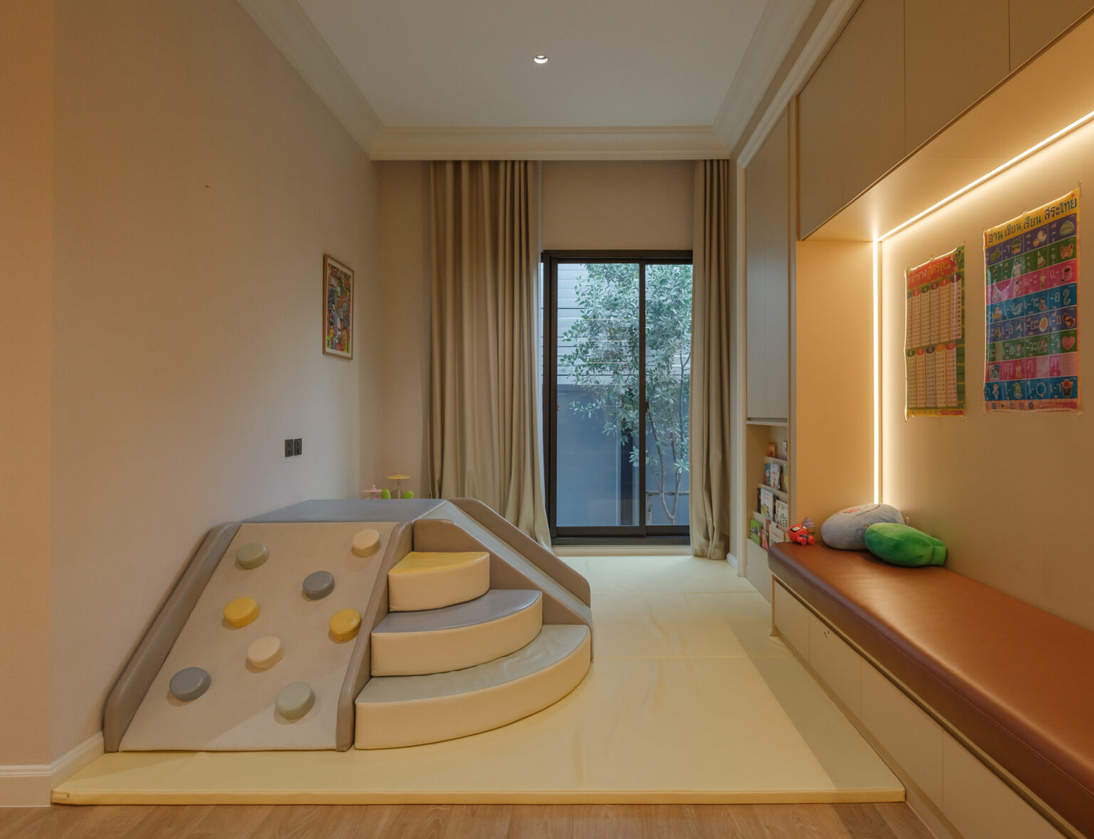 Grand Bangkok Boulevard children's playroom — soft-play climbing block on a padded floor, backlit joinery niche and leather-topped bench, interior design by Gratitude Design