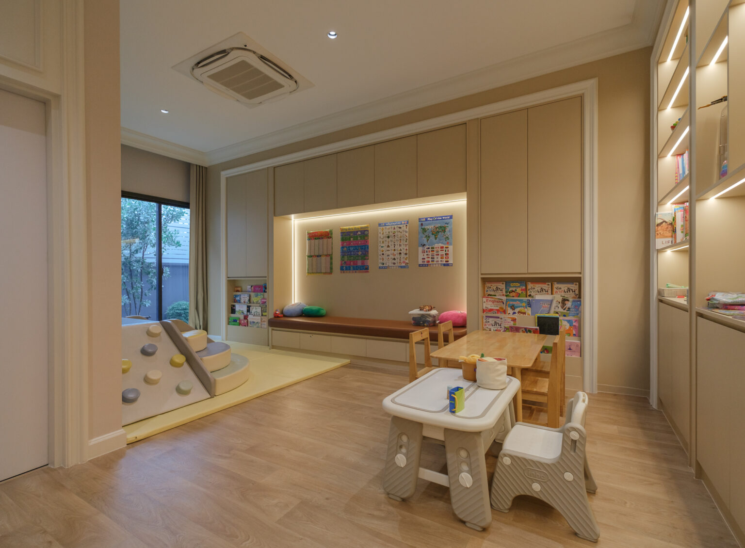 Grand Bangkok Boulevard children's playroom — built-in reading bench with book display, backlit niche, low timber table and oak floor
