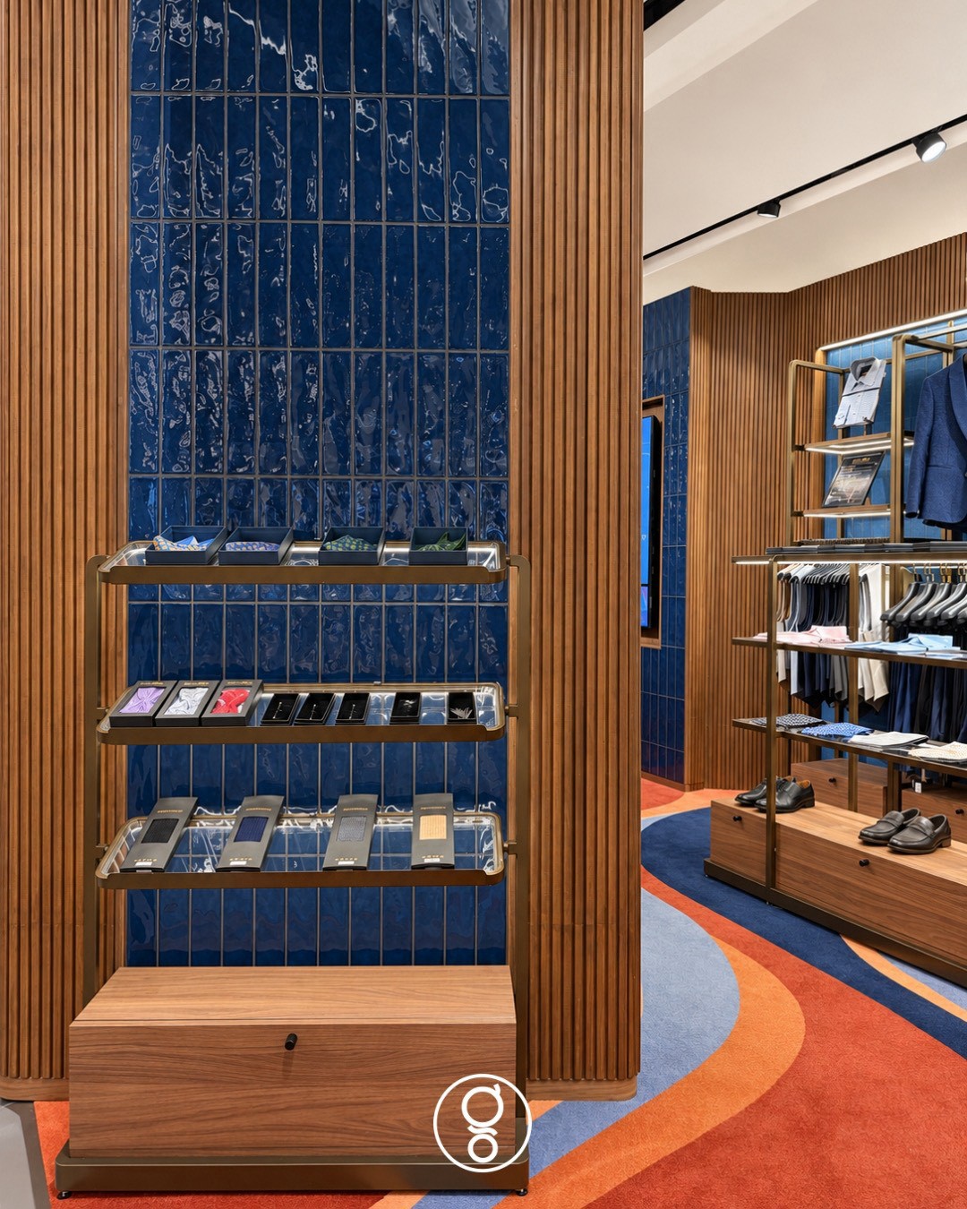 Brass-edged tie and bow-tie shelves against a column of deep-blue glazed tile framed in fluted walnut, walnut drawer plinth below