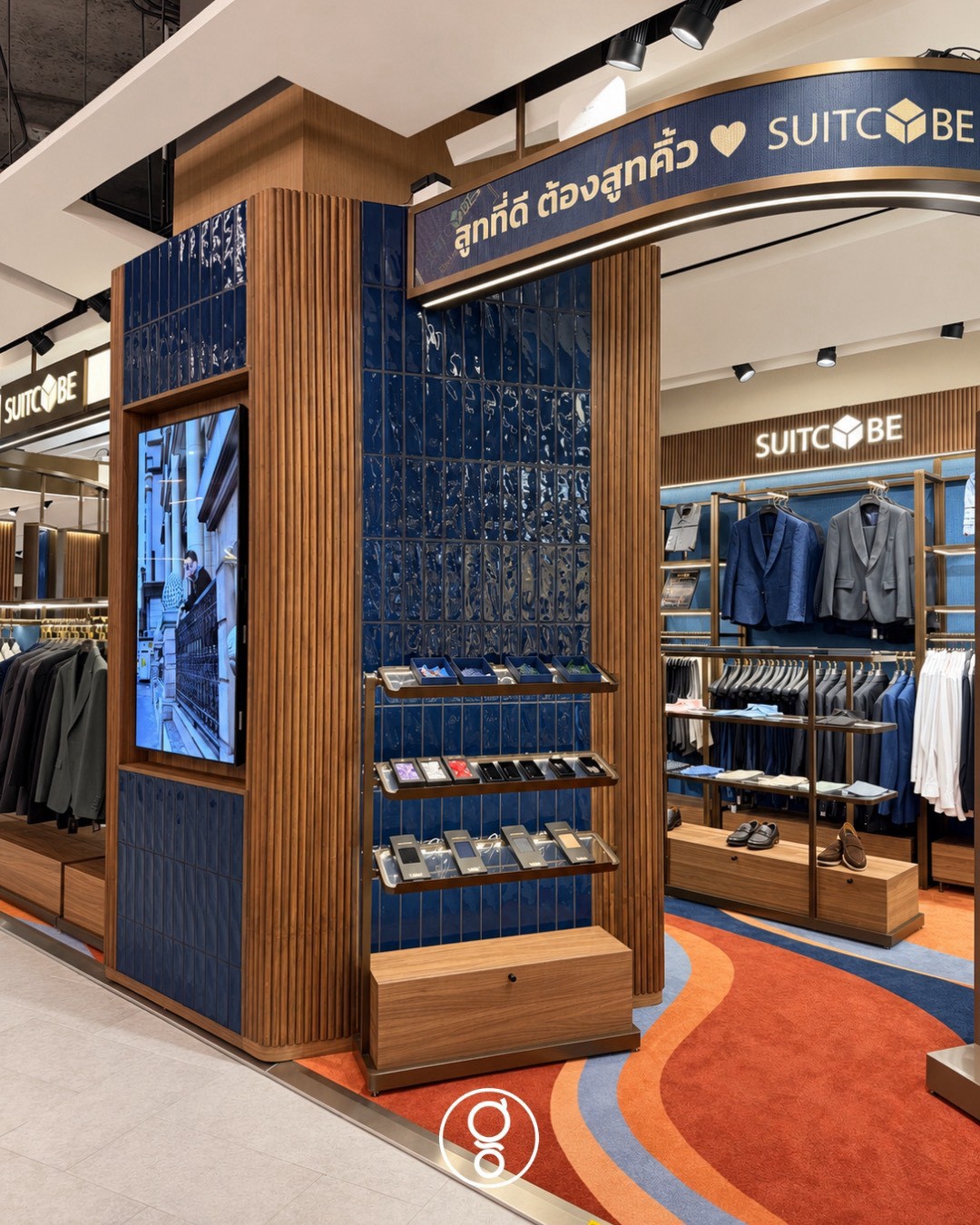 Corner pier in fluted walnut and deep-blue glazed tile with a digital screen and brass accessory shelves, curved Thai brand message above