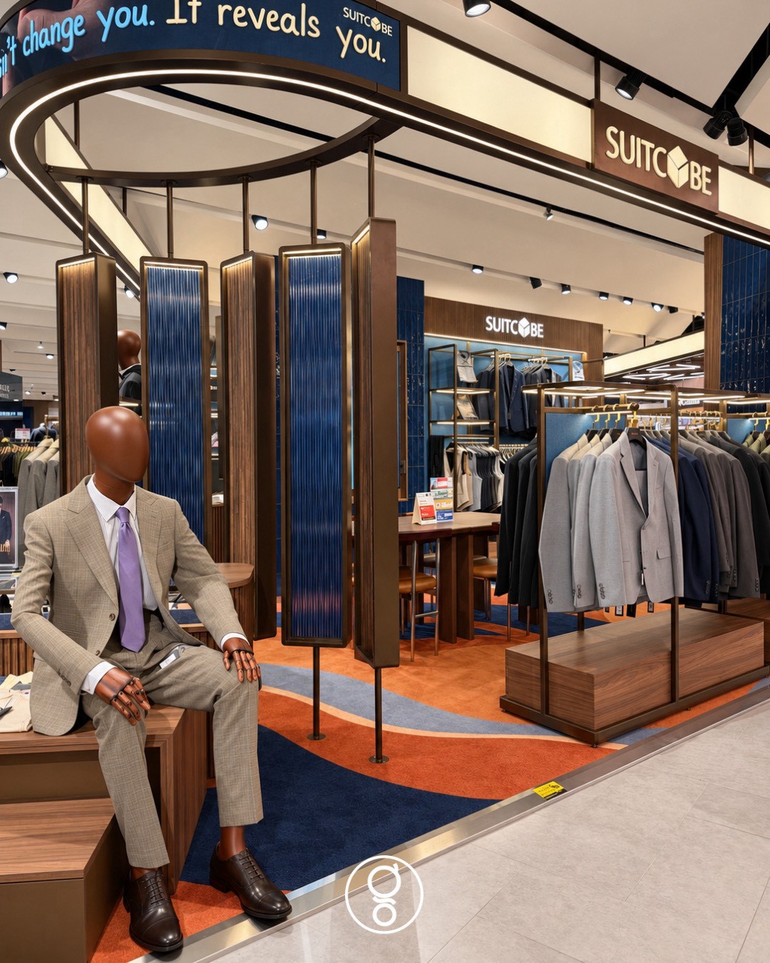 Oval brass canopy with an LED message band above hanging fluted walnut and ribbed blue glass screens, a seated mannequin in a pale suit on a walnut plinth
