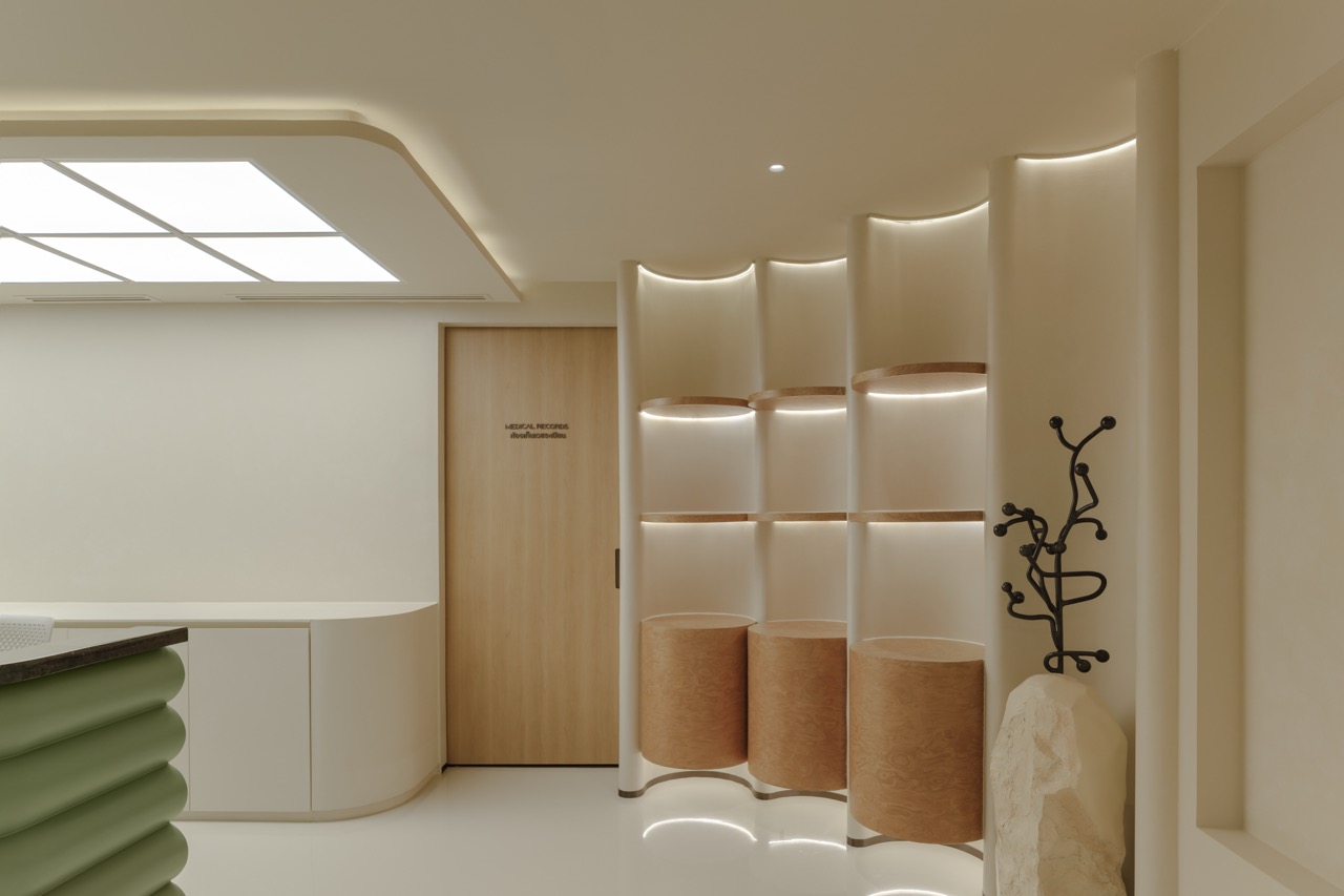 Hairtran Clinic — ชั้นโชว์ทรงโค้งซ่อนไฟพร้อมชั้นและแท่นไม้ ข้างประตูห้องเวชระเบียนและตู้ทรงมน