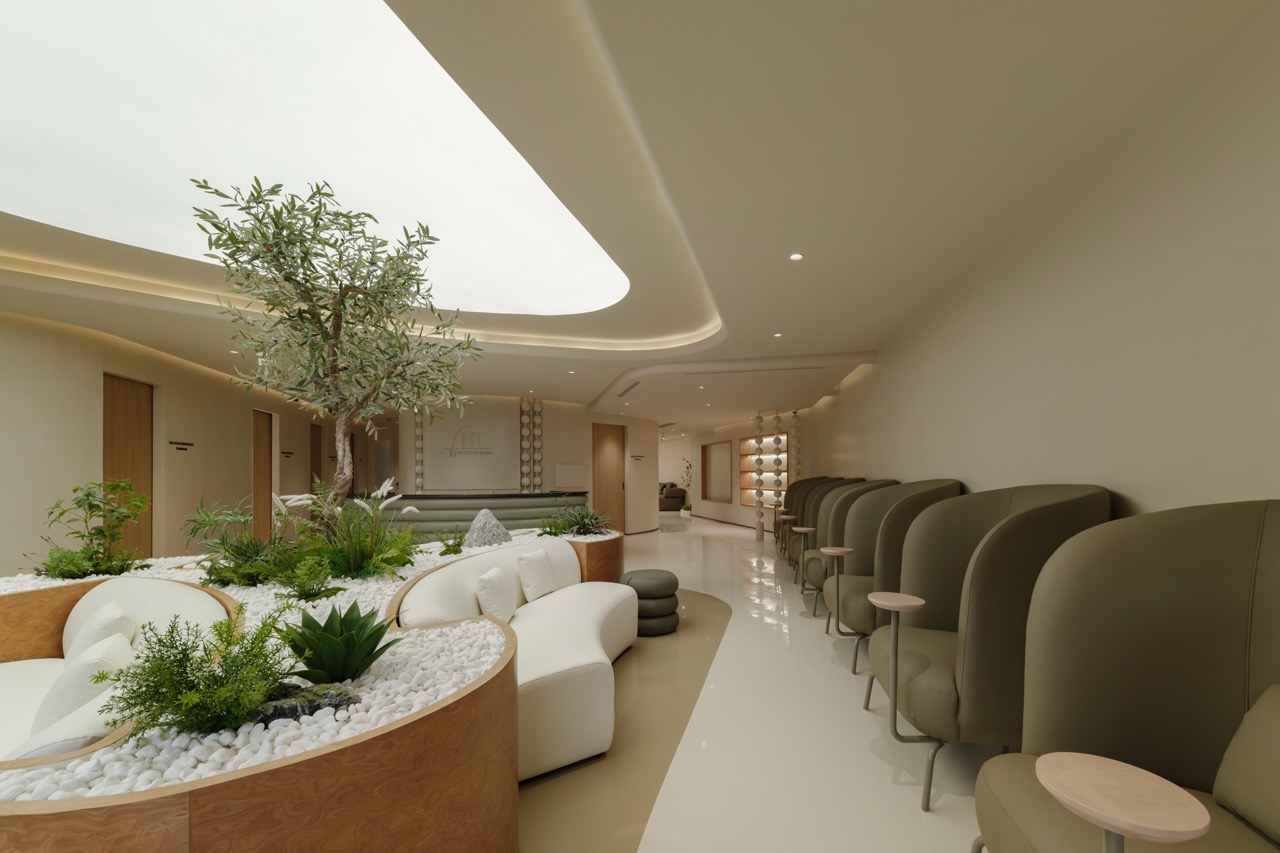 ส่วนพักคอย Hairtran Clinic — โซฟาโค้งรอบกระบะต้นไม้และต้นมะกอก แถวเก้าอี้เลานจ์สีเขียวเซจ และส่วนต้อนรับด้านหลัง