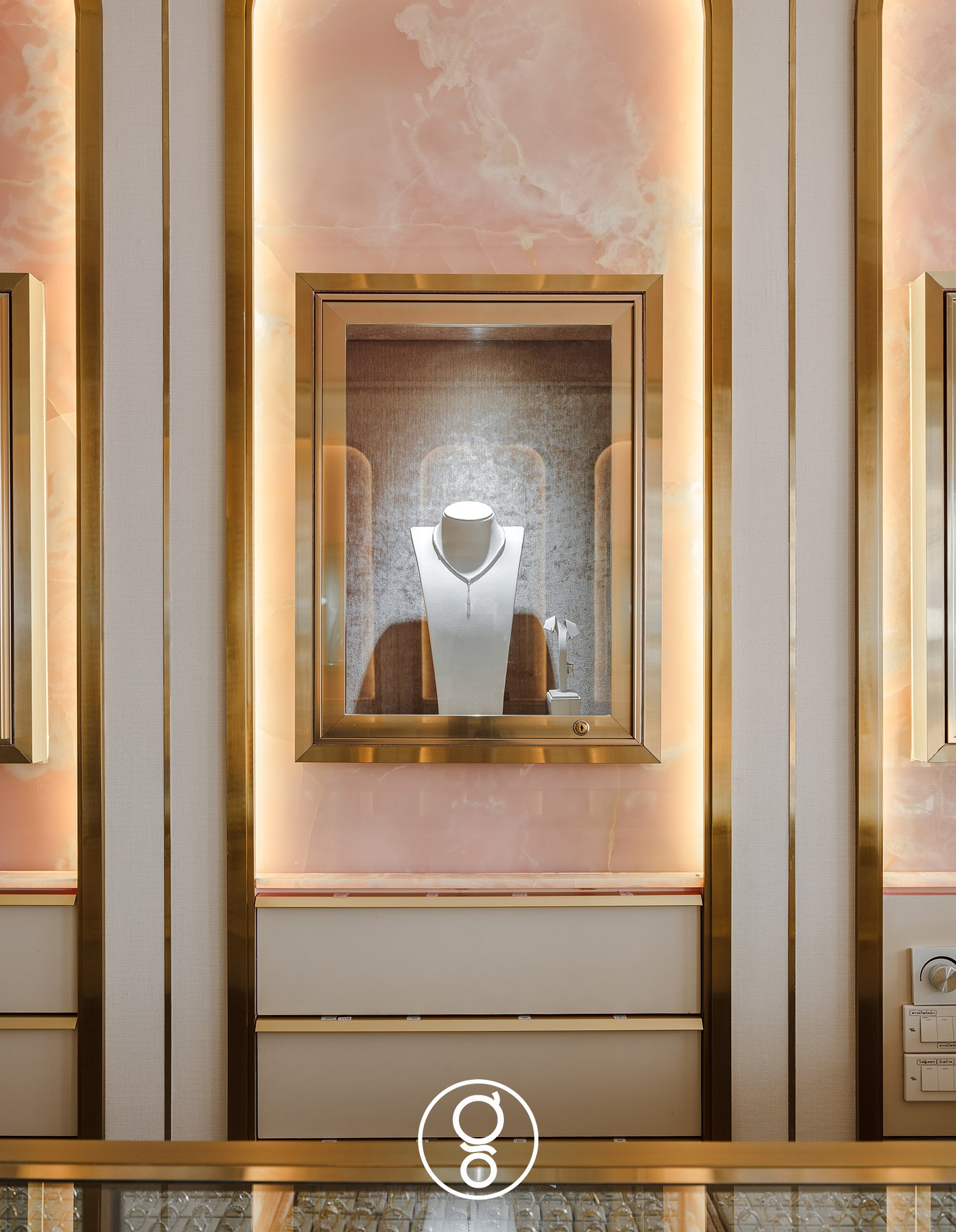 A brass-framed display niche with a necklace bust against backlit pink onyx at Nopparat Jewelry