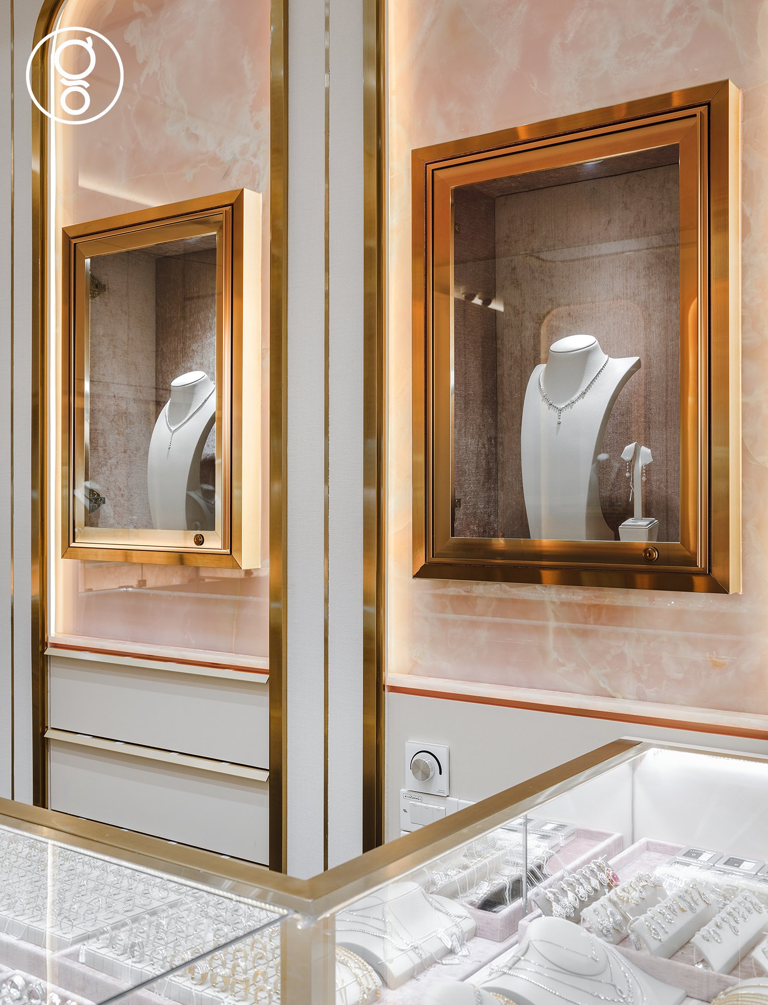 Brass-framed display niches set into backlit pink onyx at Nopparat Jewelry, with a glass counter of rings and earrings below