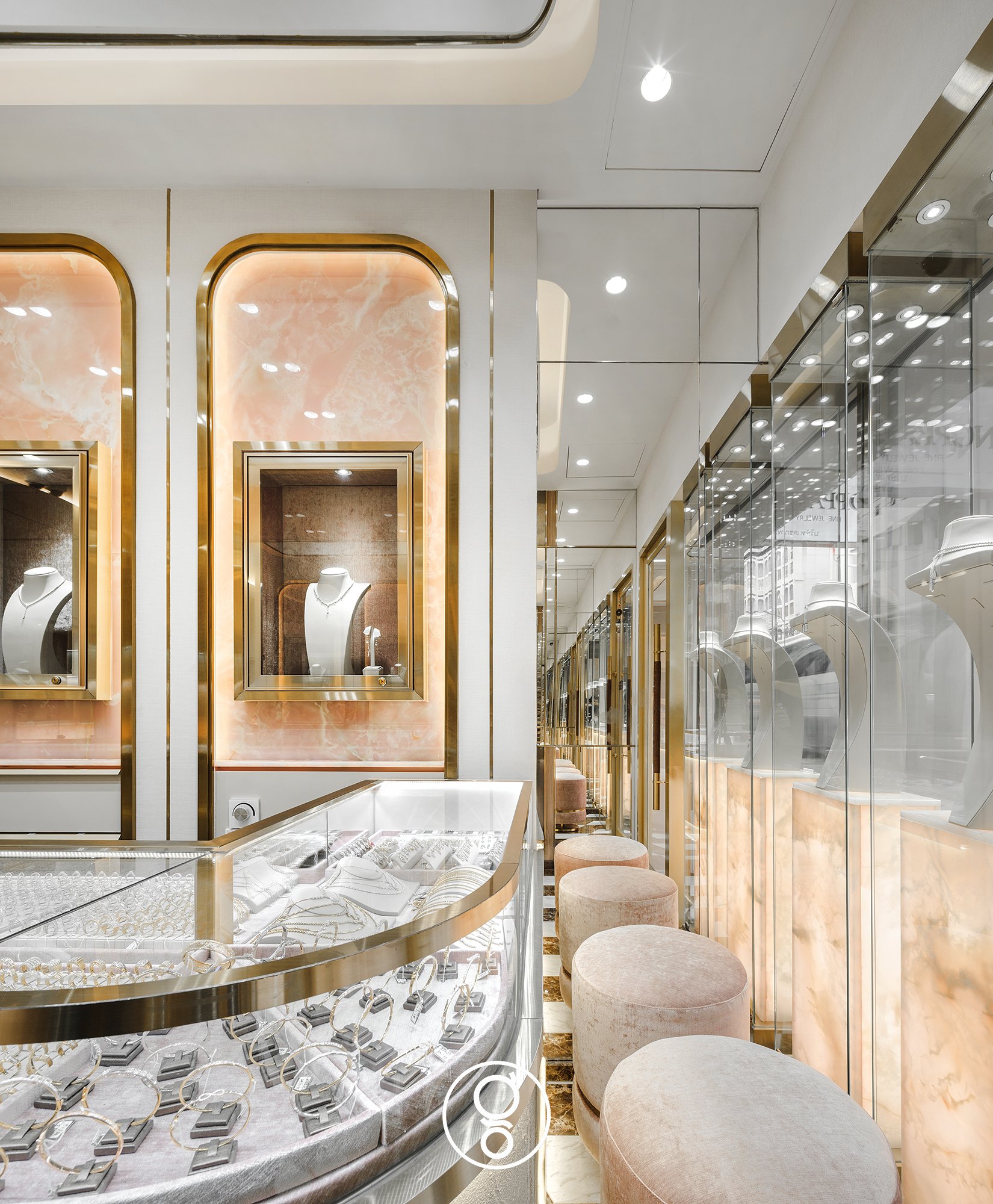 Nopparat Jewelry — a curved brass-edged glass counter, blush velvet stools and glass window showcases with necklace busts on backlit onyx plinths