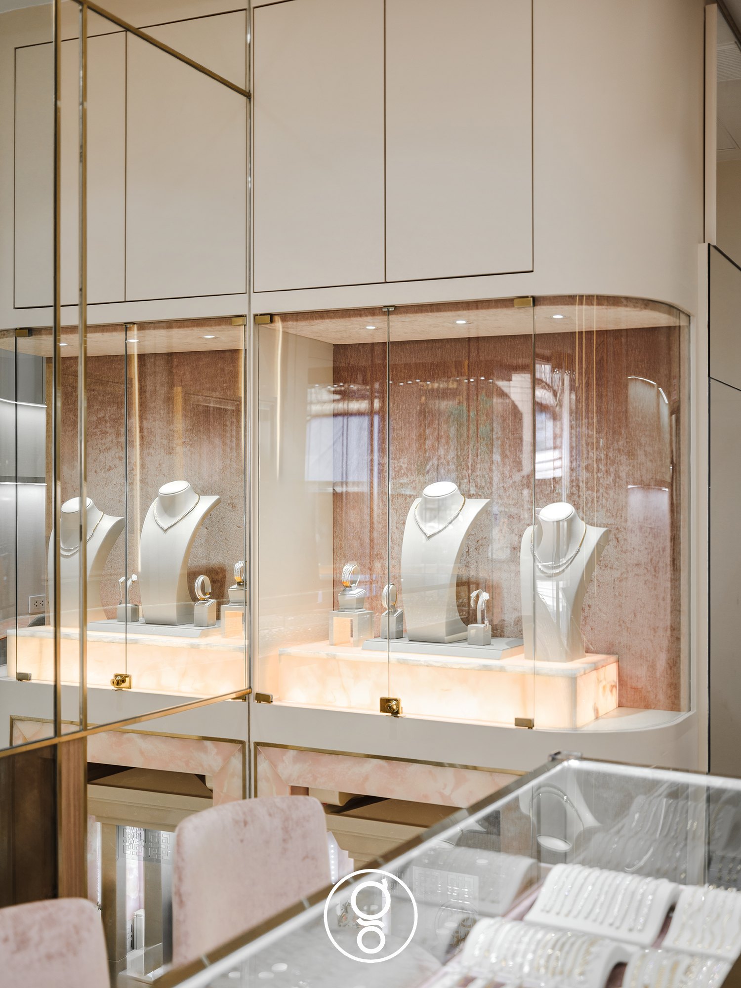 A curved glass showcase at Nopparat Jewelry with necklace busts on backlit onyx plinths against a blush textured backdrop
