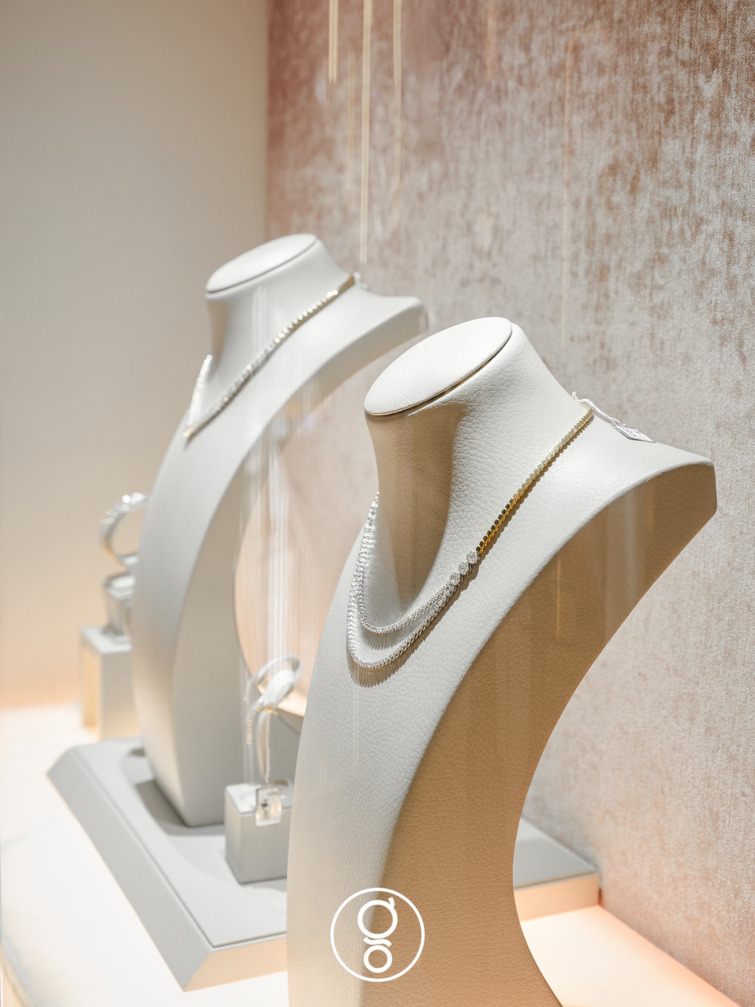 Necklace busts on a lit plinth against a blush textured backdrop at Nopparat Jewelry