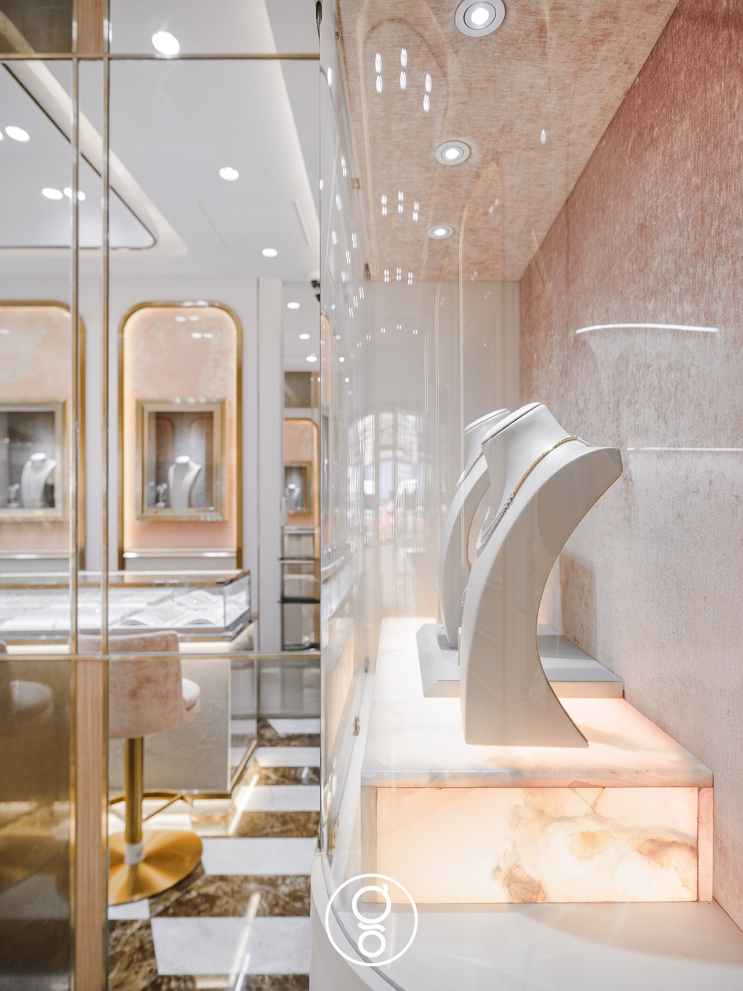 Side view of a glass showcase at Nopparat Jewelry with necklace busts on a backlit onyx plinth, the arched niches reflected beyond