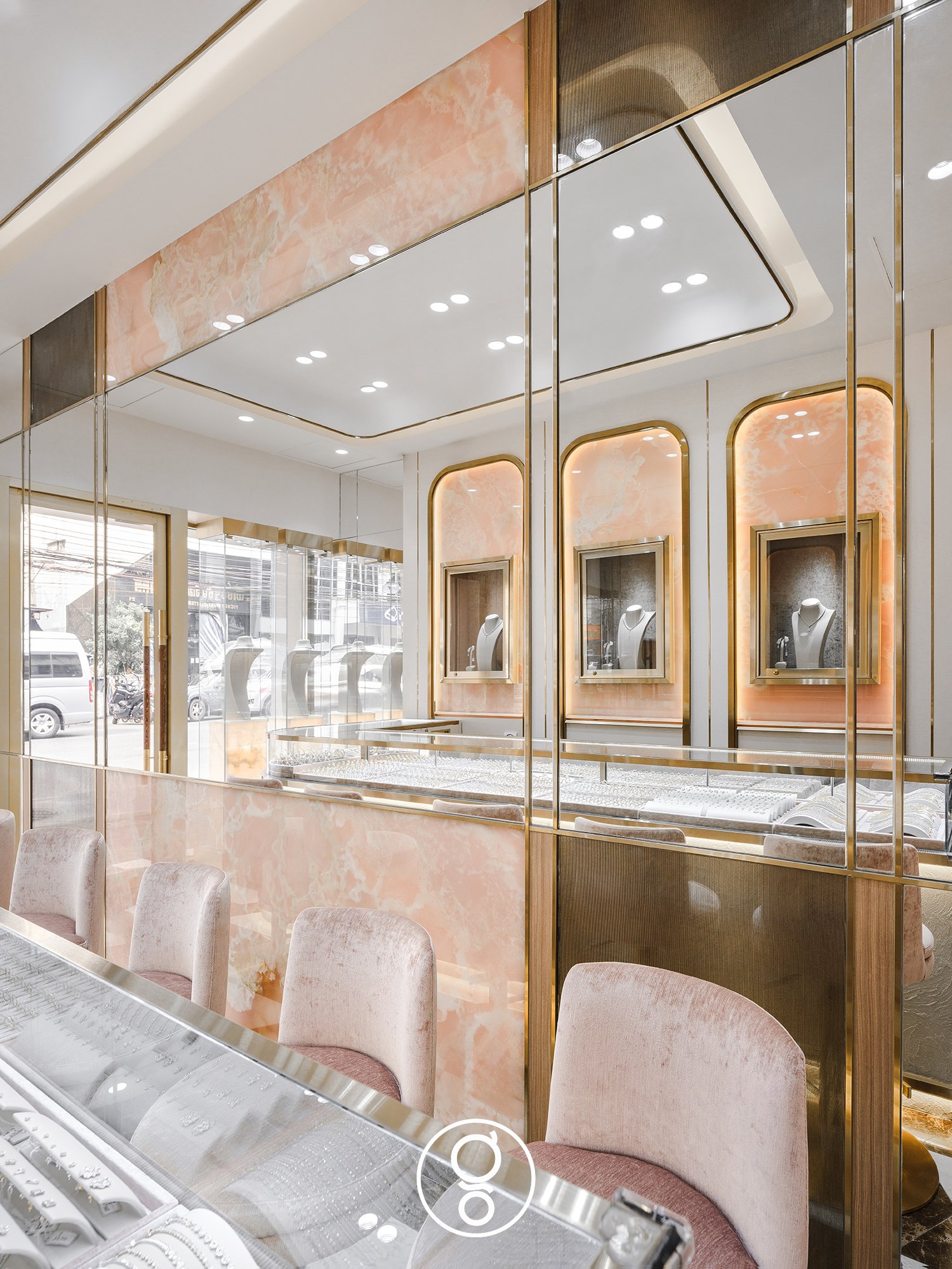 Nopparat Jewelry — a mirrored wall with brass dividers above a pink onyx panel and blush velvet stools at the glass counter