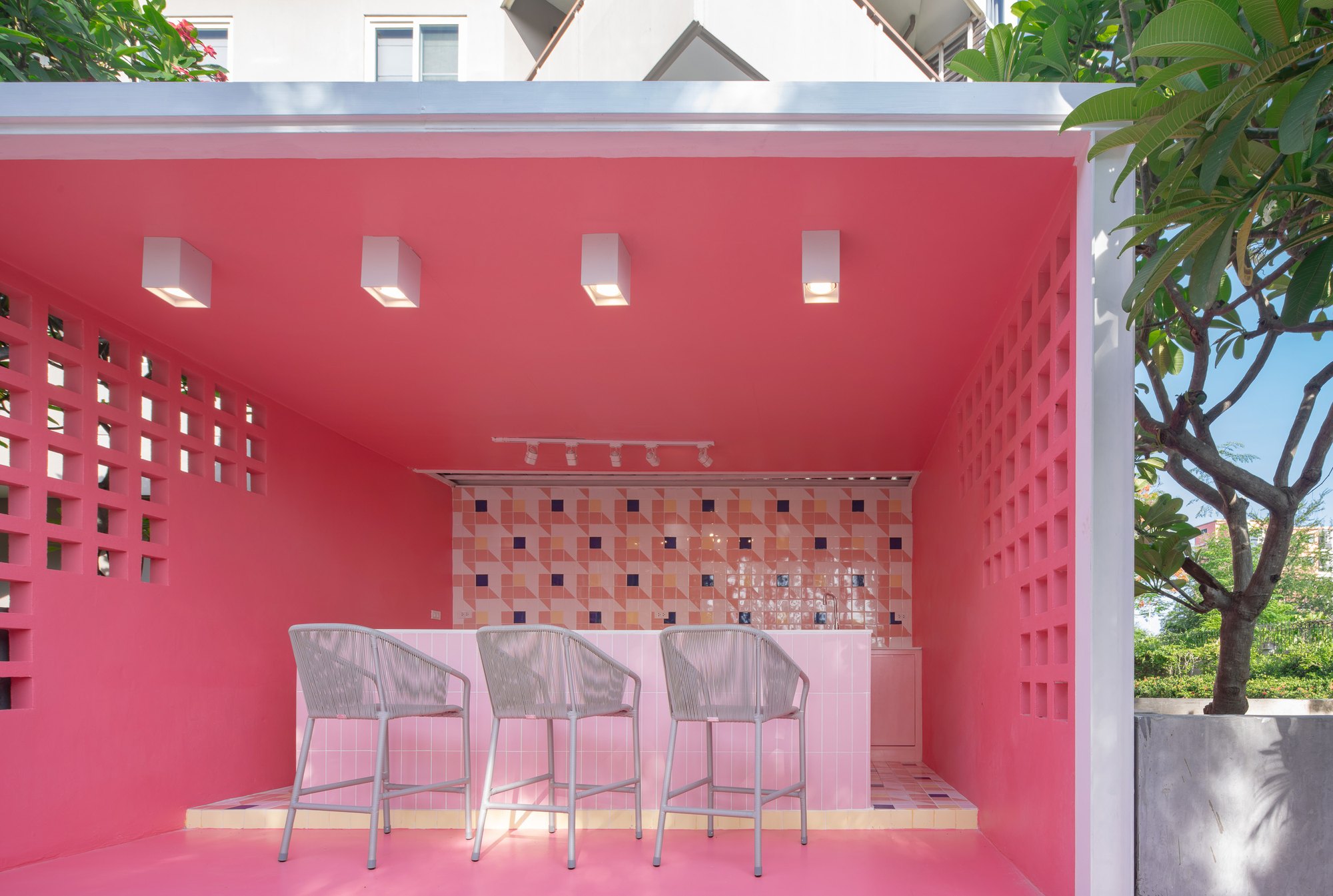 Sala Huahin bar pavilion — a coral pink box with breeze-block side walls, three rope bar stools at a pink tiled counter and a geometric tiled backsplash