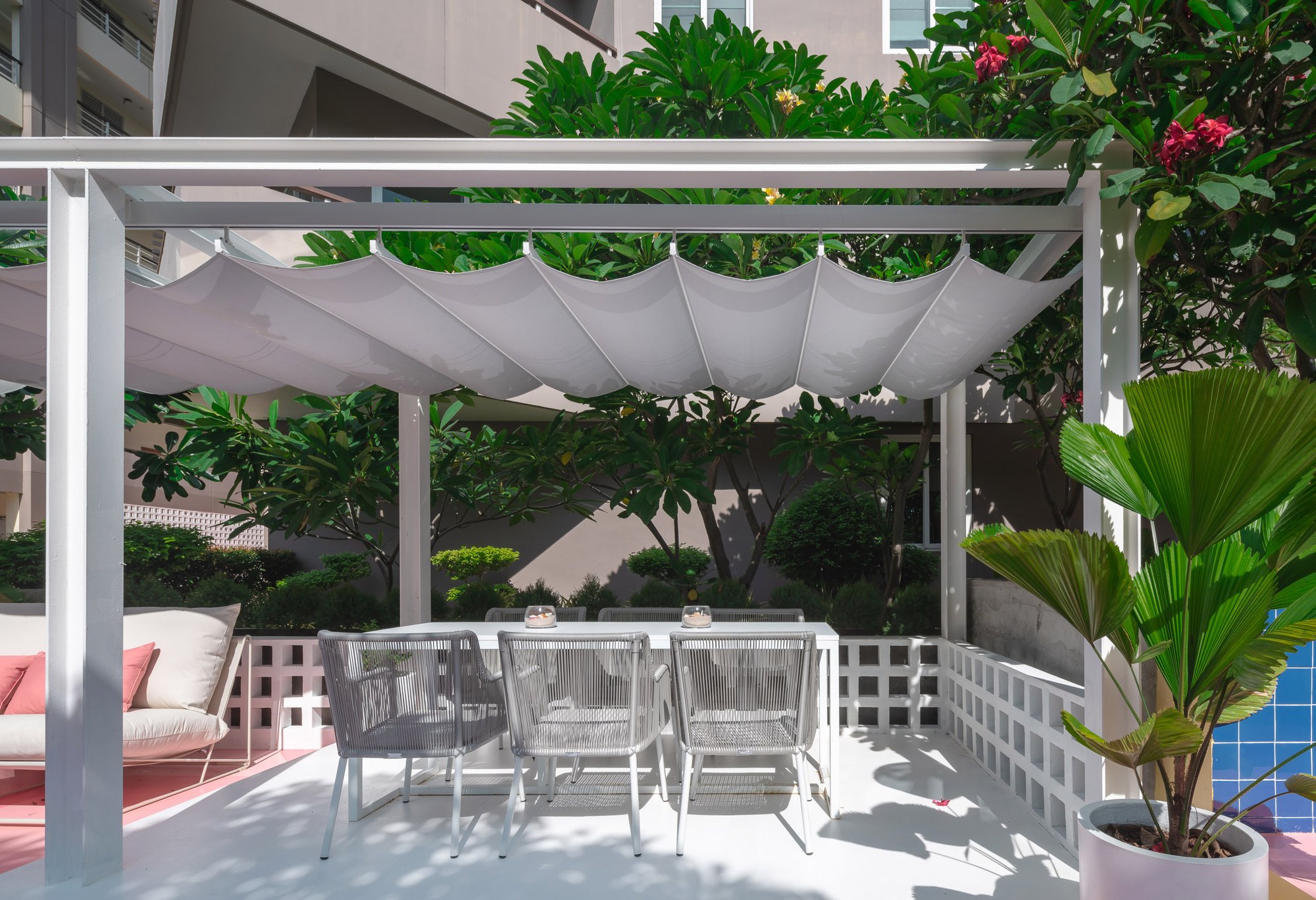 Shaded dining pavilion at Sala Huahin — a white table with rope chairs under a pleated fabric canopy, framed by white breeze blocks and frangipani trees