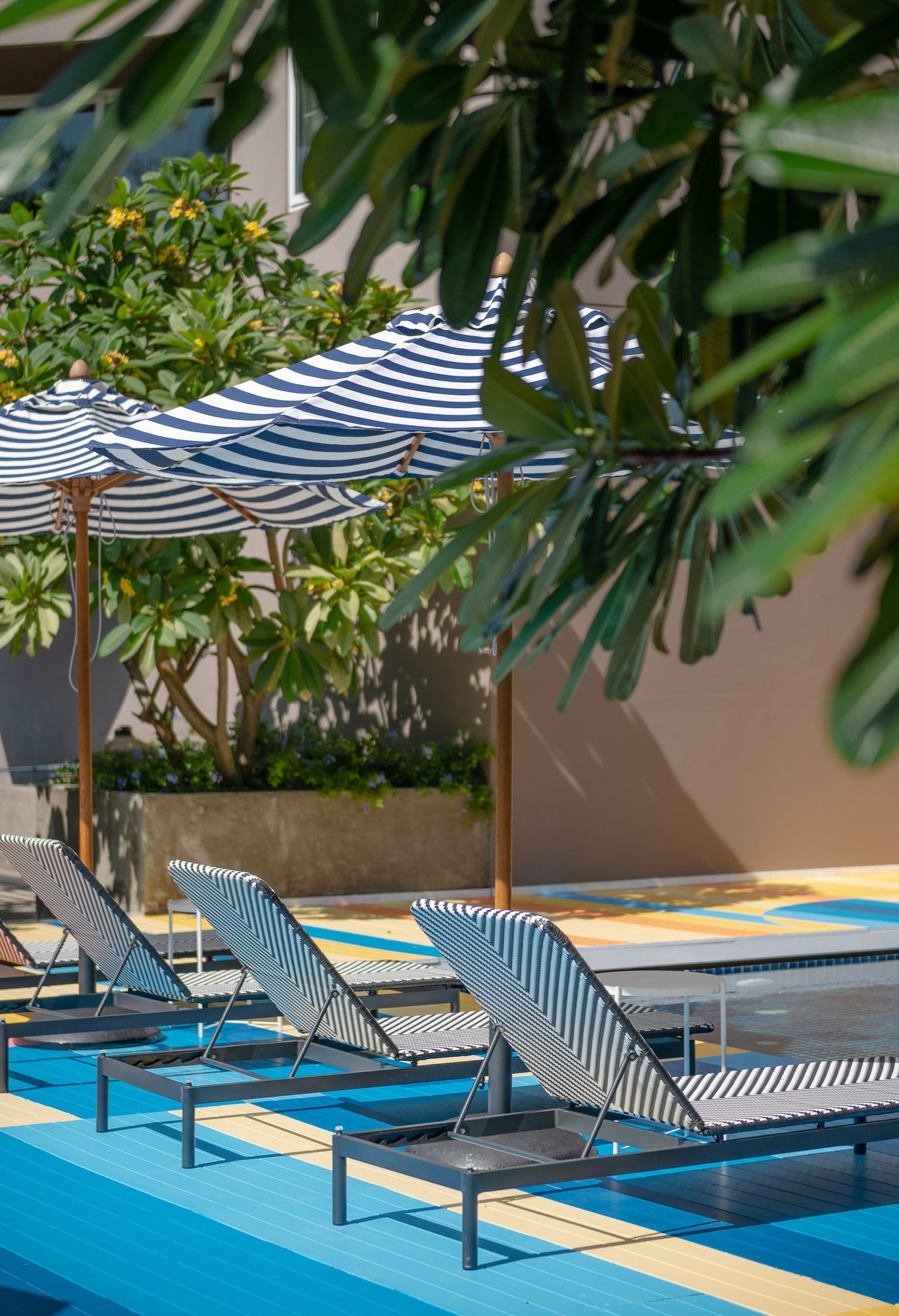 Black and white woven loungers under striped parasols on the blue and yellow painted deck at Sala Huahin