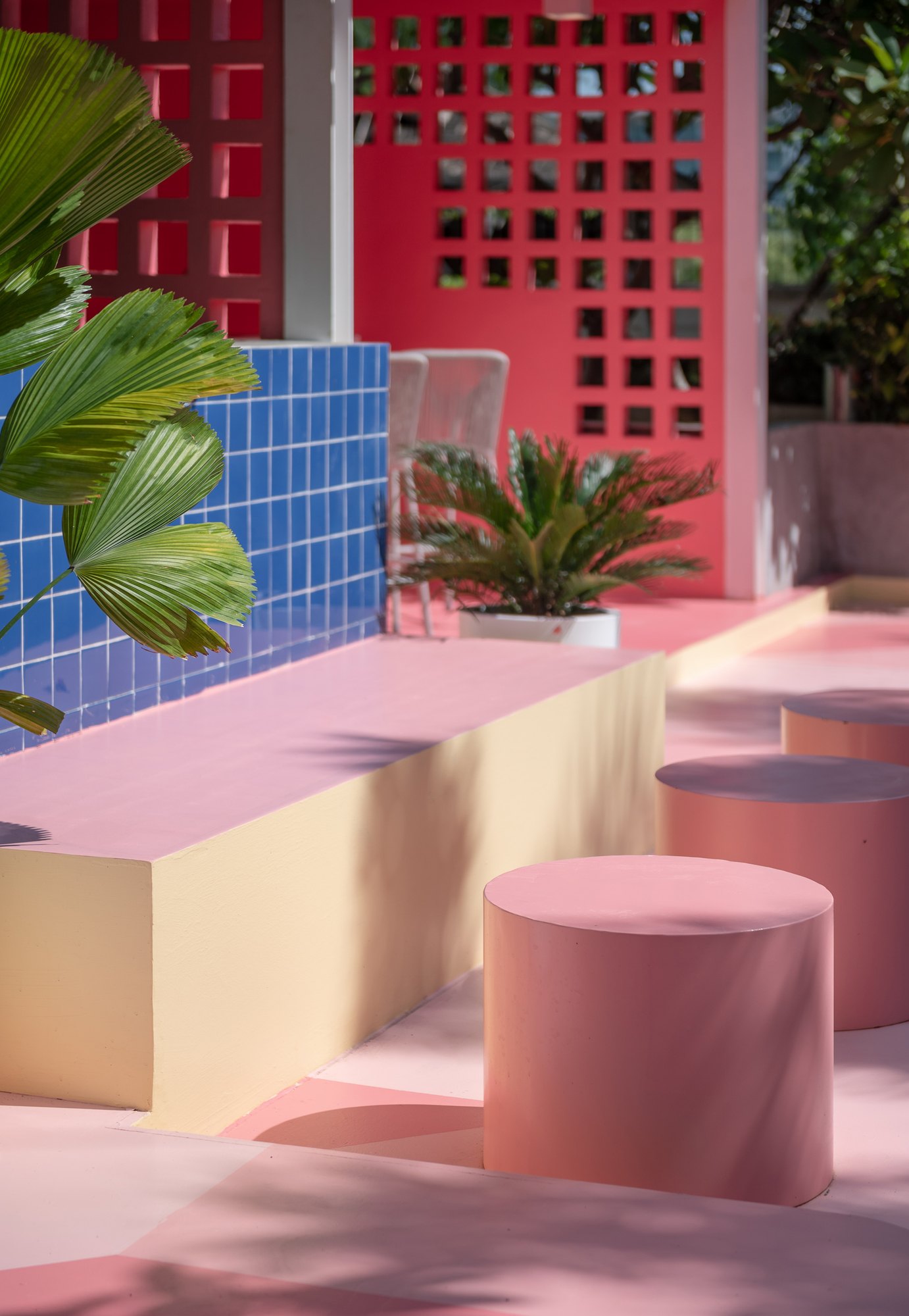 Round pink stools and a yellow-sided bench against a blue tiled wall and the pink breeze-block bar at Sala Huahin