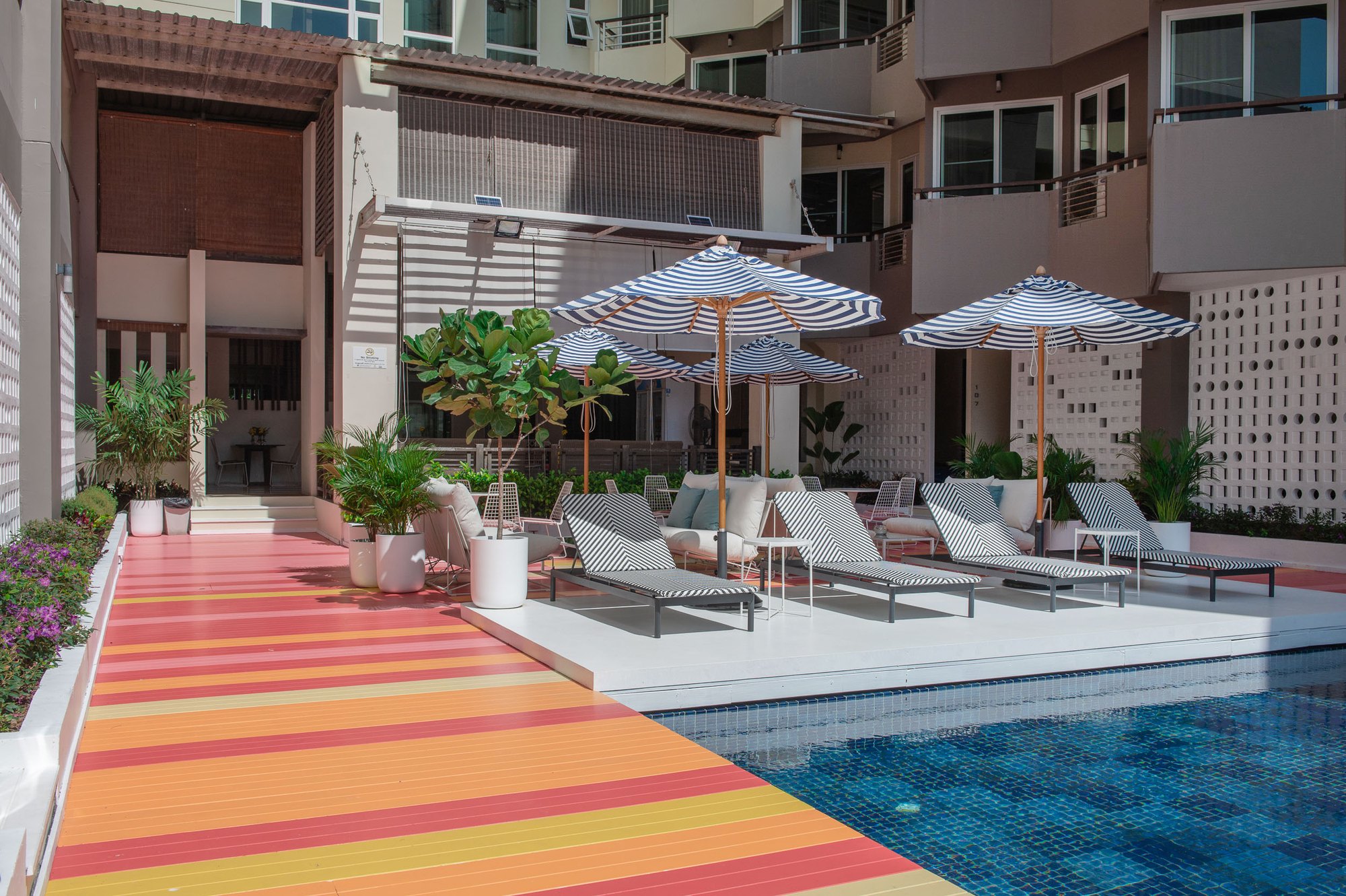 Sala Huahin — a poolside lounge with parasols, loungers and white sofas on a coral and orange striped deck, before the hotel building