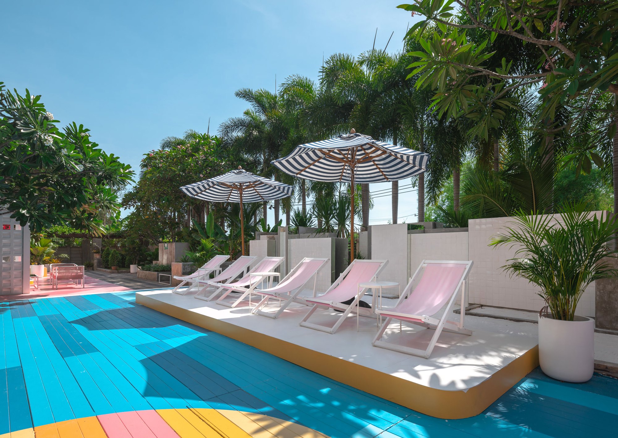Sala Huahin — pink deck chairs on a curved white platform under striped parasols, the blue painted deck in front and palms behind