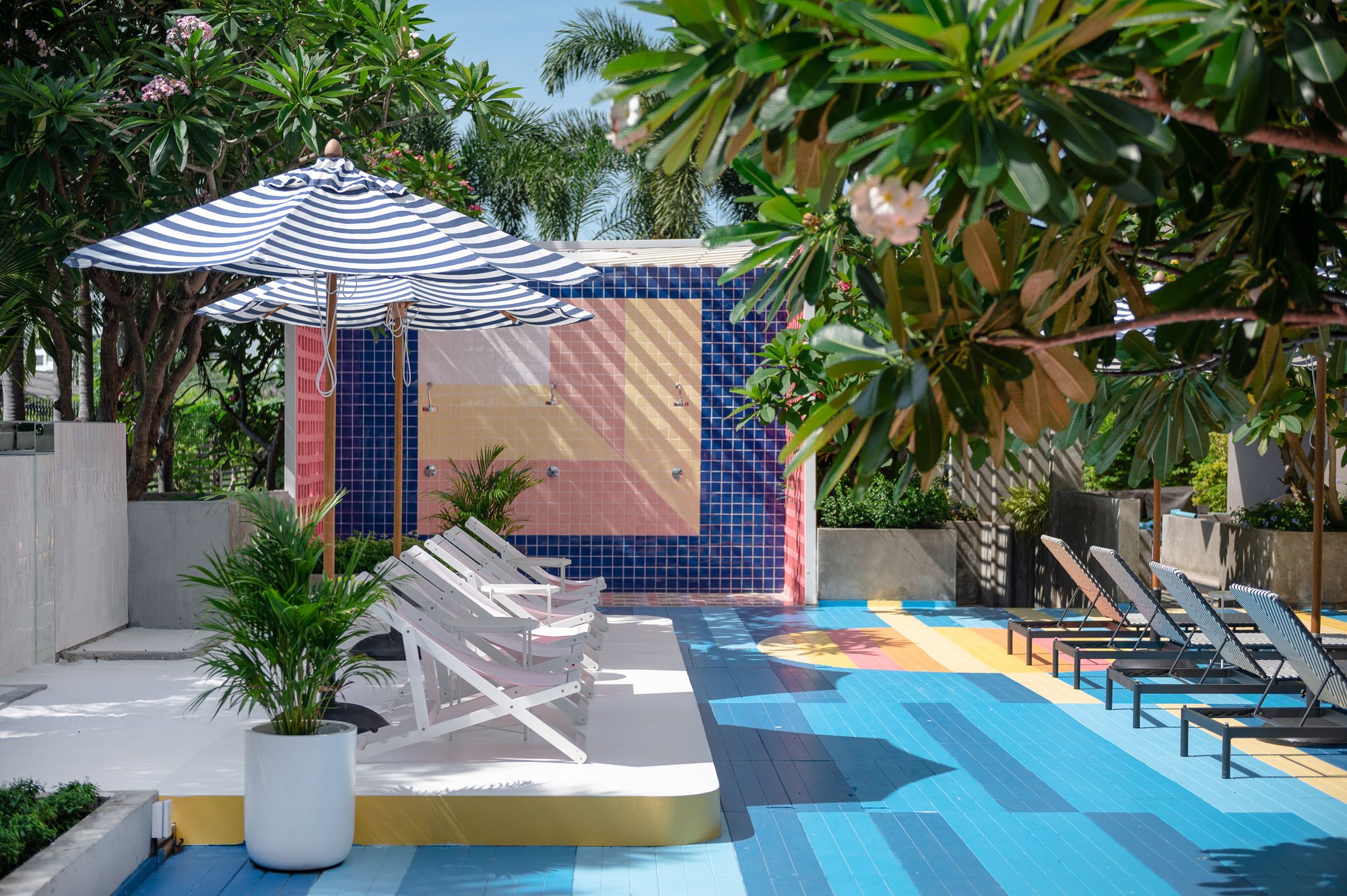 Sala Huahin — the tiled outdoor shower wall in navy, pink and yellow, pink deck chairs under striped parasols and loungers on the painted deck