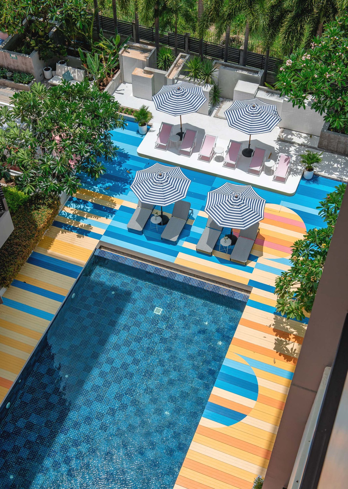 Sala Huahin from above — the pool, deck painted in stripes and half circles of blue, yellow, orange and pink, striped parasols and a white platform of pink deck chairs